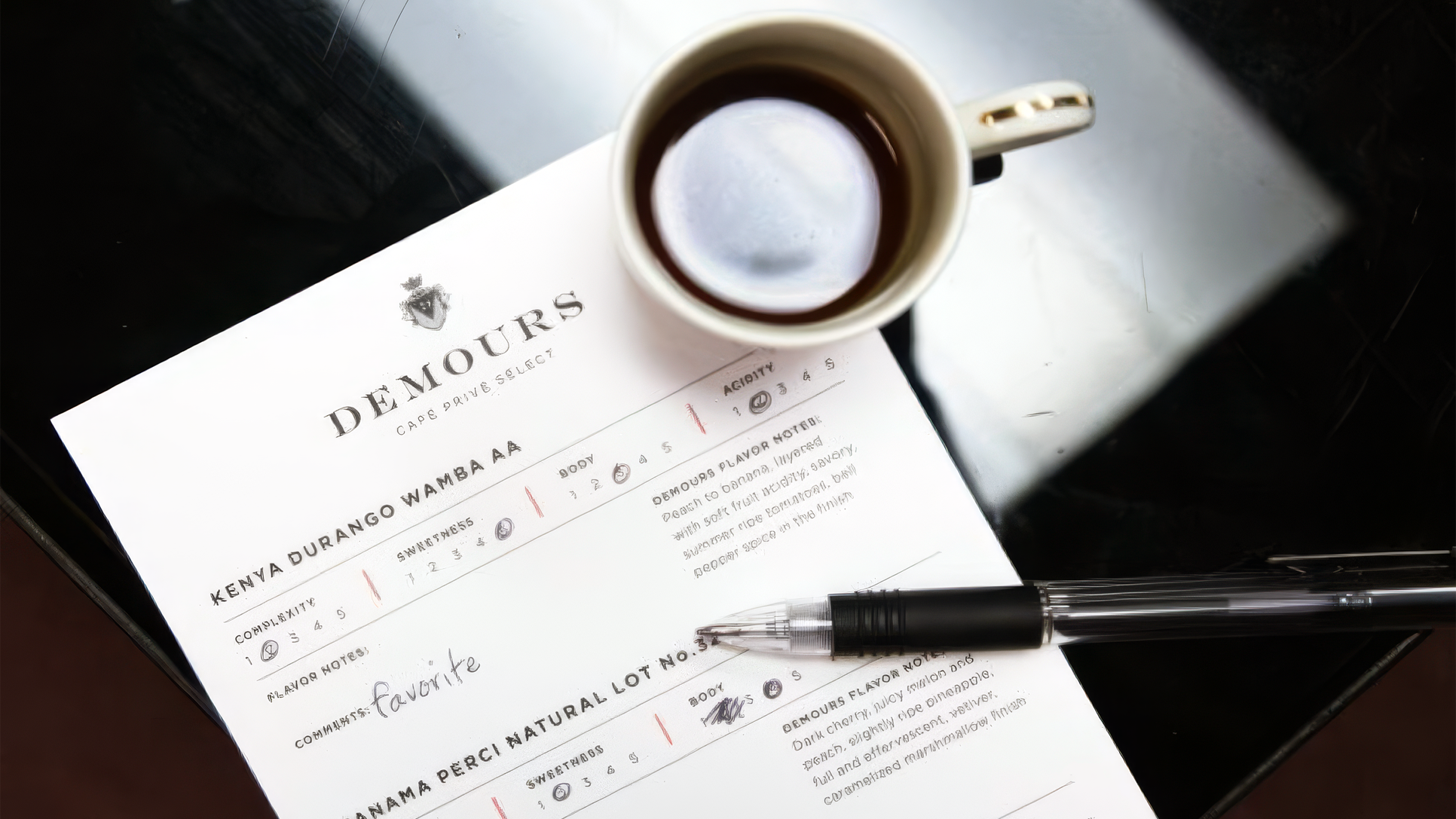 Demours Coffee tasting-notes sheet beside a pen and coffee cup.