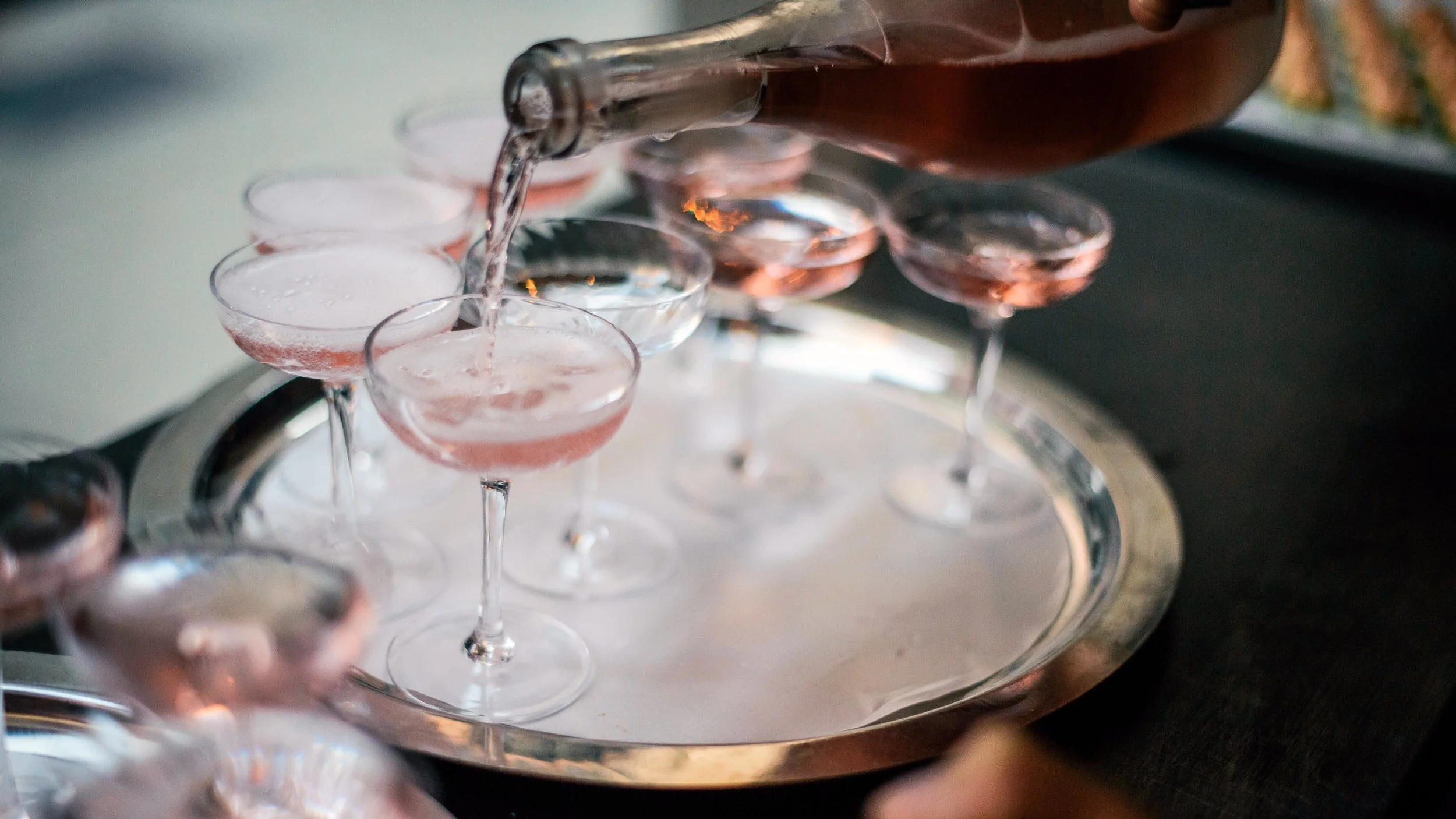Pink sparkling wine poured into coupe glasses on a silver serving tray at Measure.