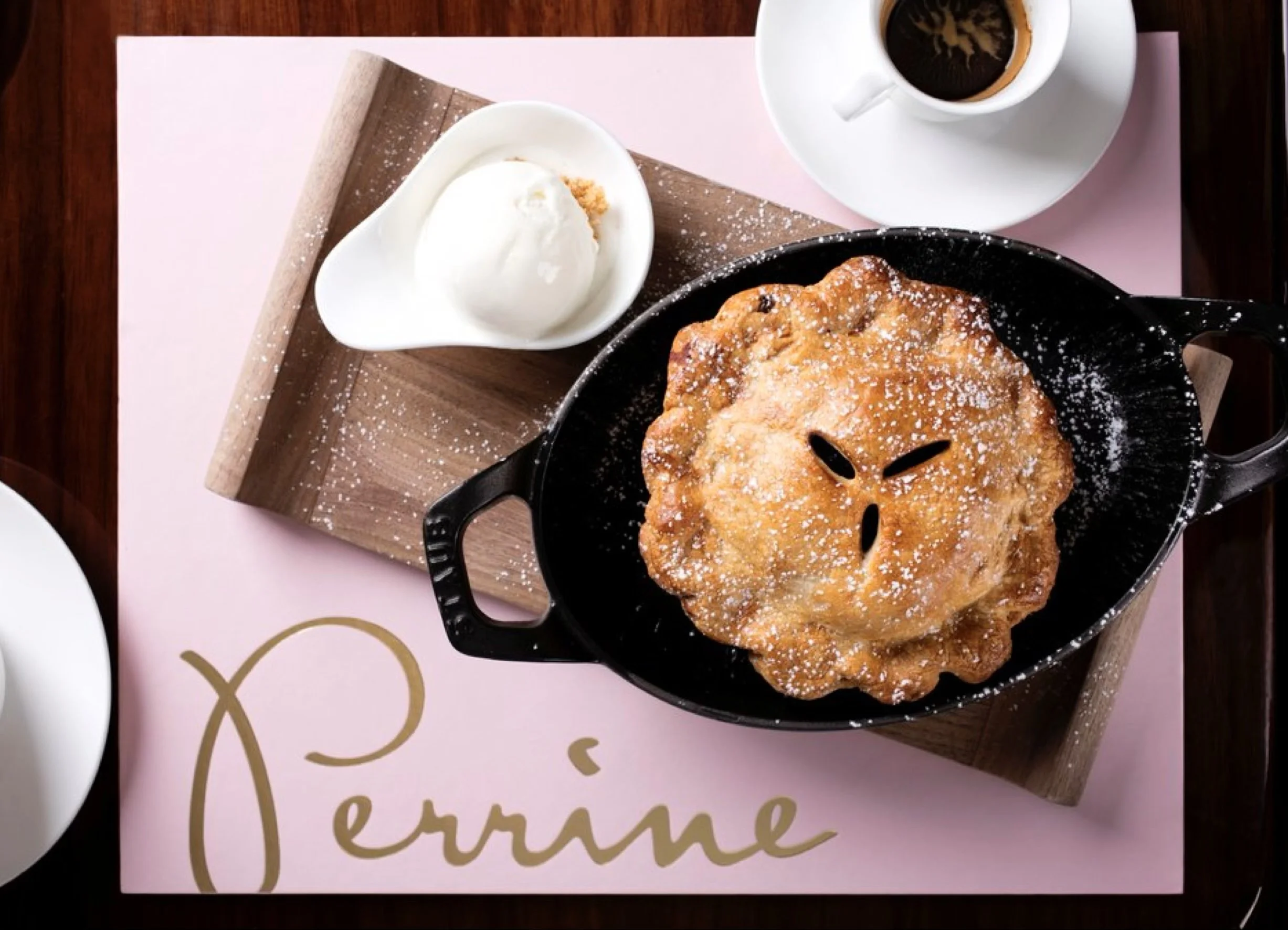 Overhead view of a baked dessert in a skillet on a pale pink Perrine-branded table mat.