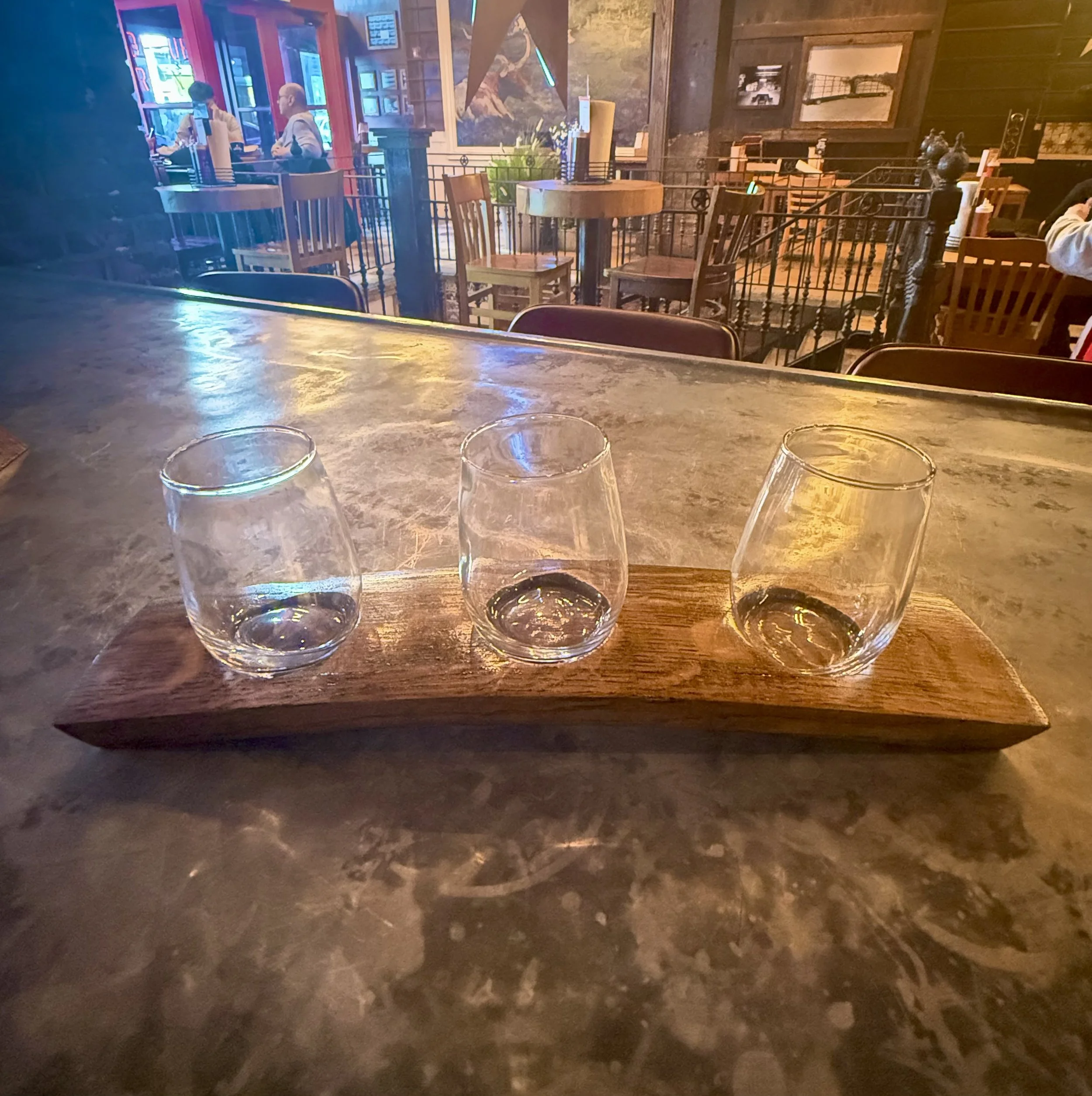 Source photograph of three empty tasting glasses on a wooden paddle at the Hill Country bar.