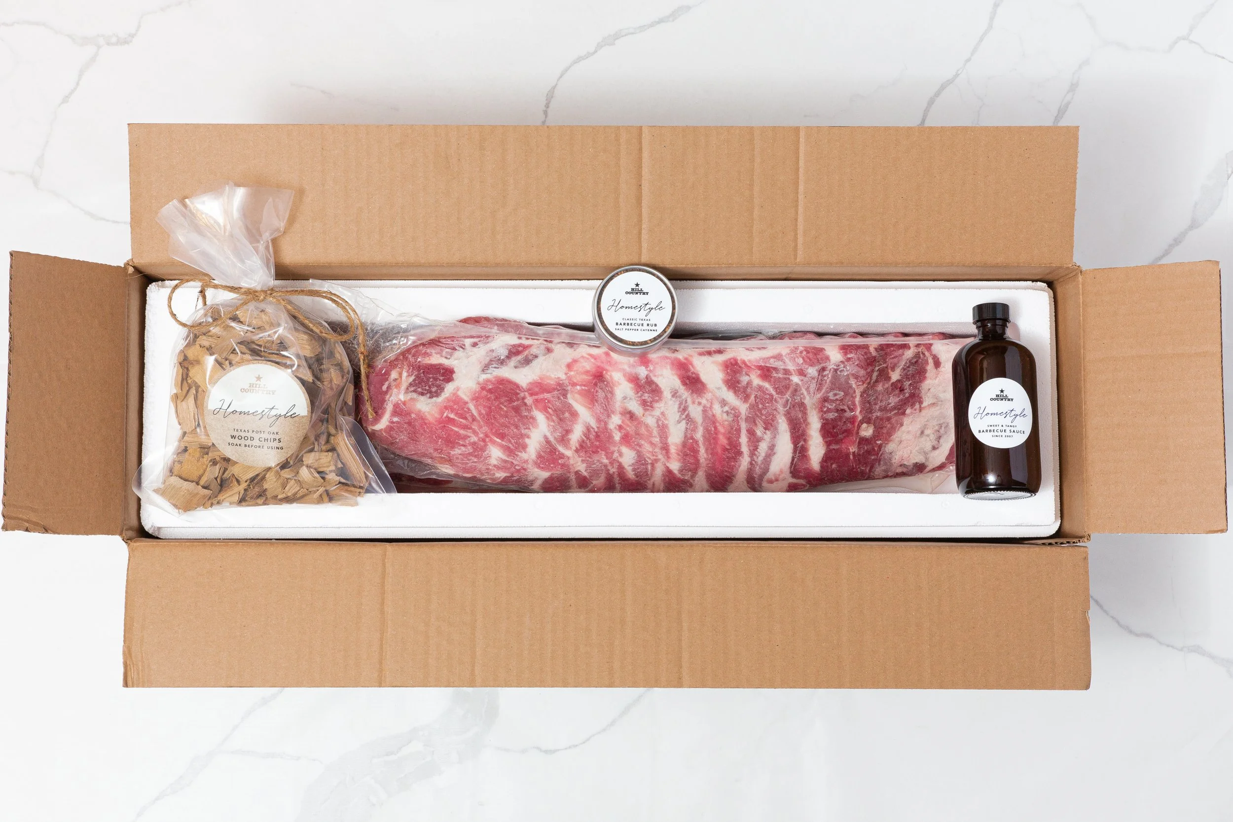 Hill Country Homestyle rib kit in an open insulated box with ribs, seasoning, sauce and smoking chips.