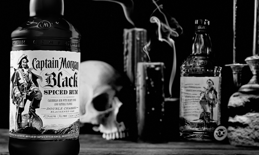 Captain Morgan Black bottles photographed in a dark still life with a skull, smoking pipe and candlesticks.
