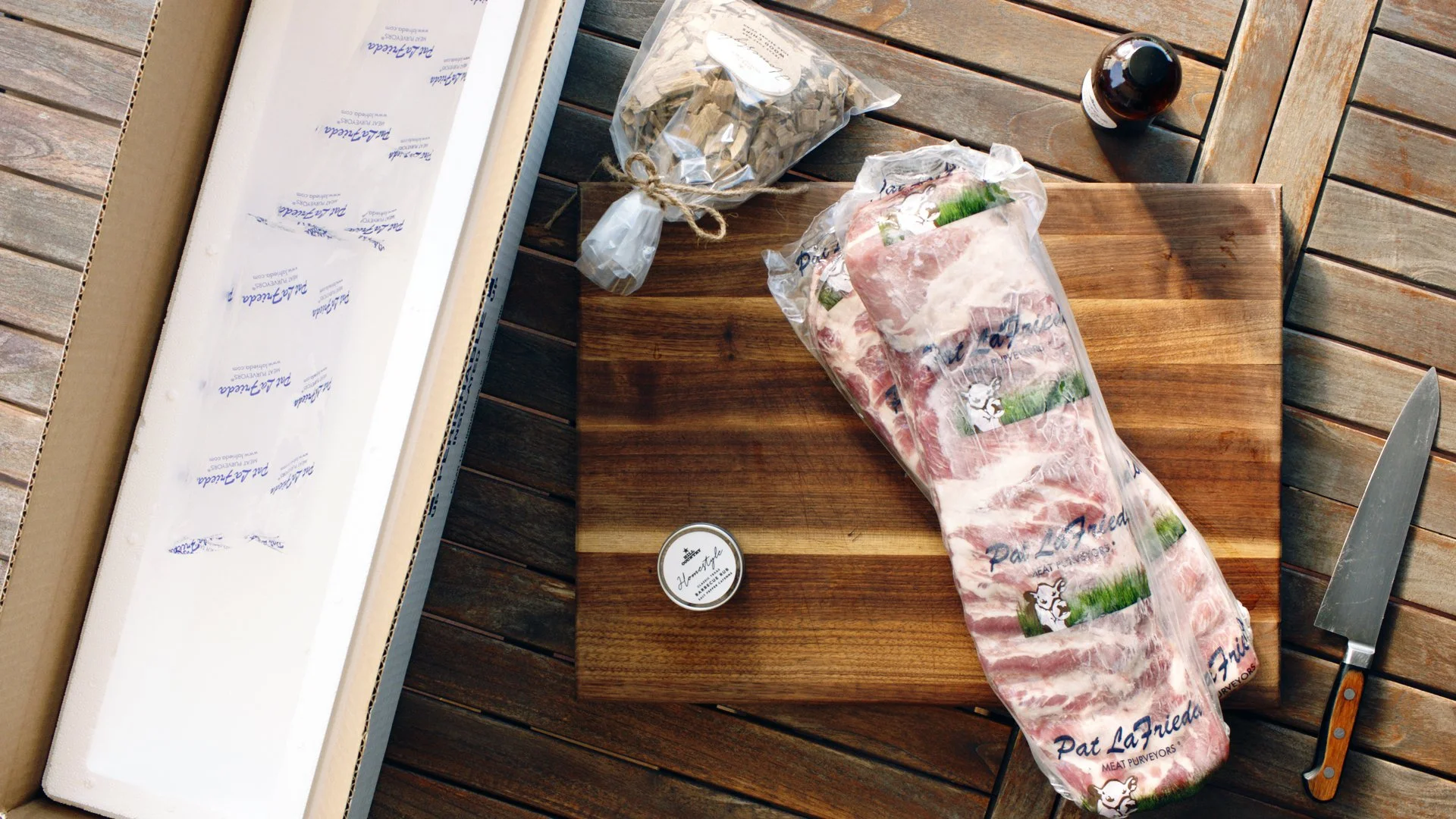 Hill Country rib-kit contents being unpacked on an outdoor table, with wrapped ribs, seasoning and smoking chips.