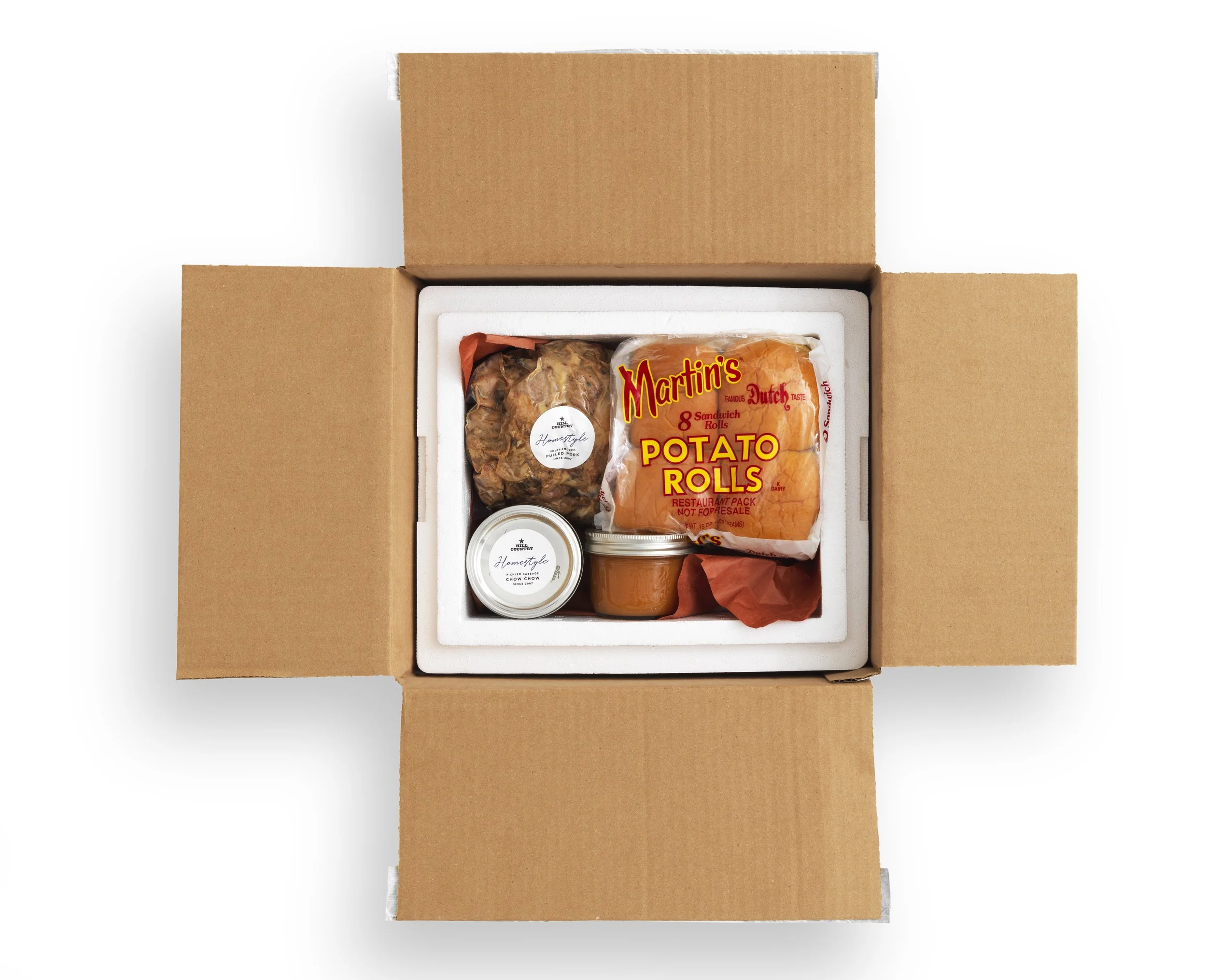 Open Hill Country Homestyle food-delivery box with potato rolls, packaged meat and condiment containers.