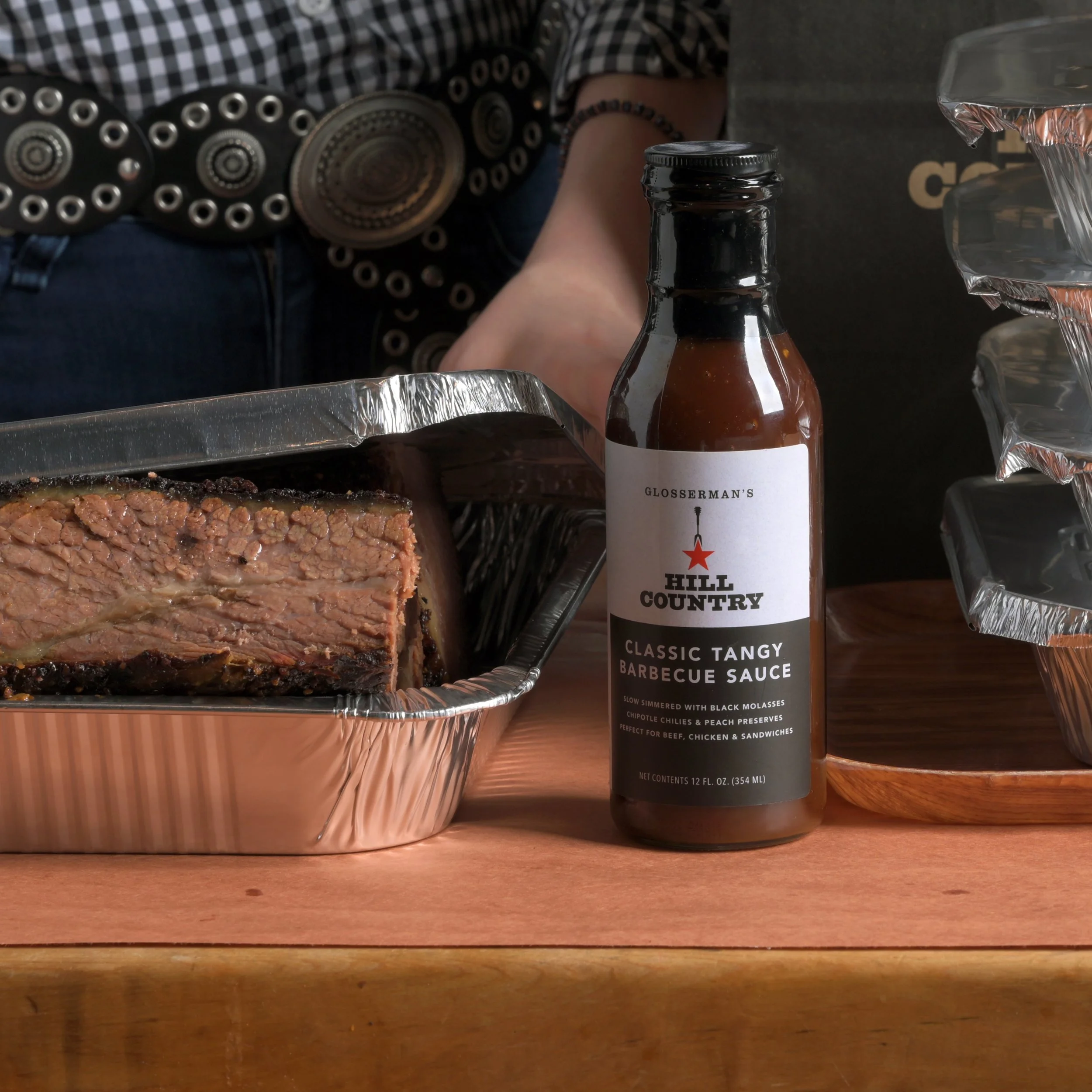 Finished Hill Country Classic Tangy Barbecue Sauce bottle beside a tray of brisket.