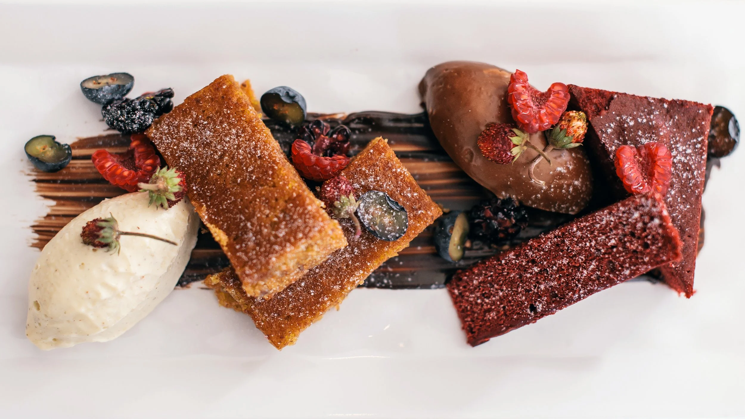 Measure dessert presentation with pastries, berries and scoops of cream on a rectangular white plate.