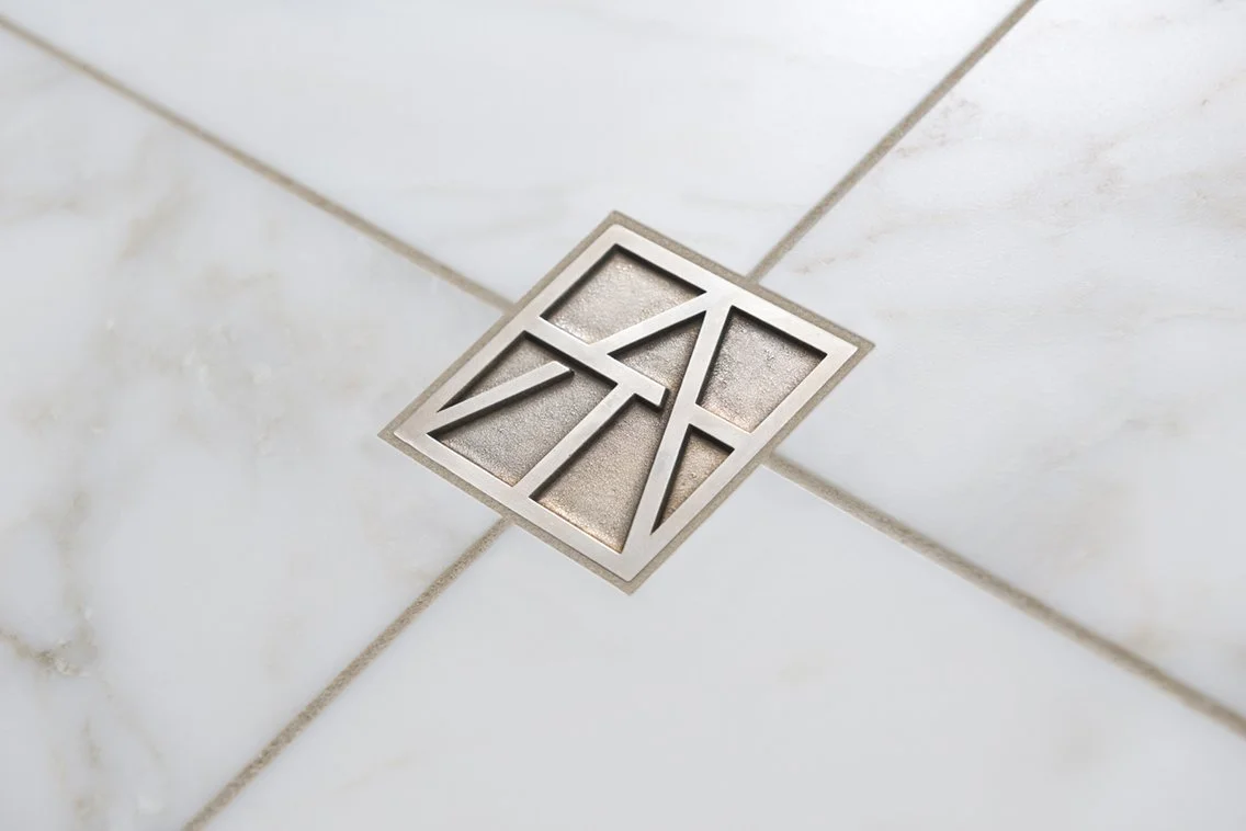 Artistic Tile metallic monogram set into white marble tile.