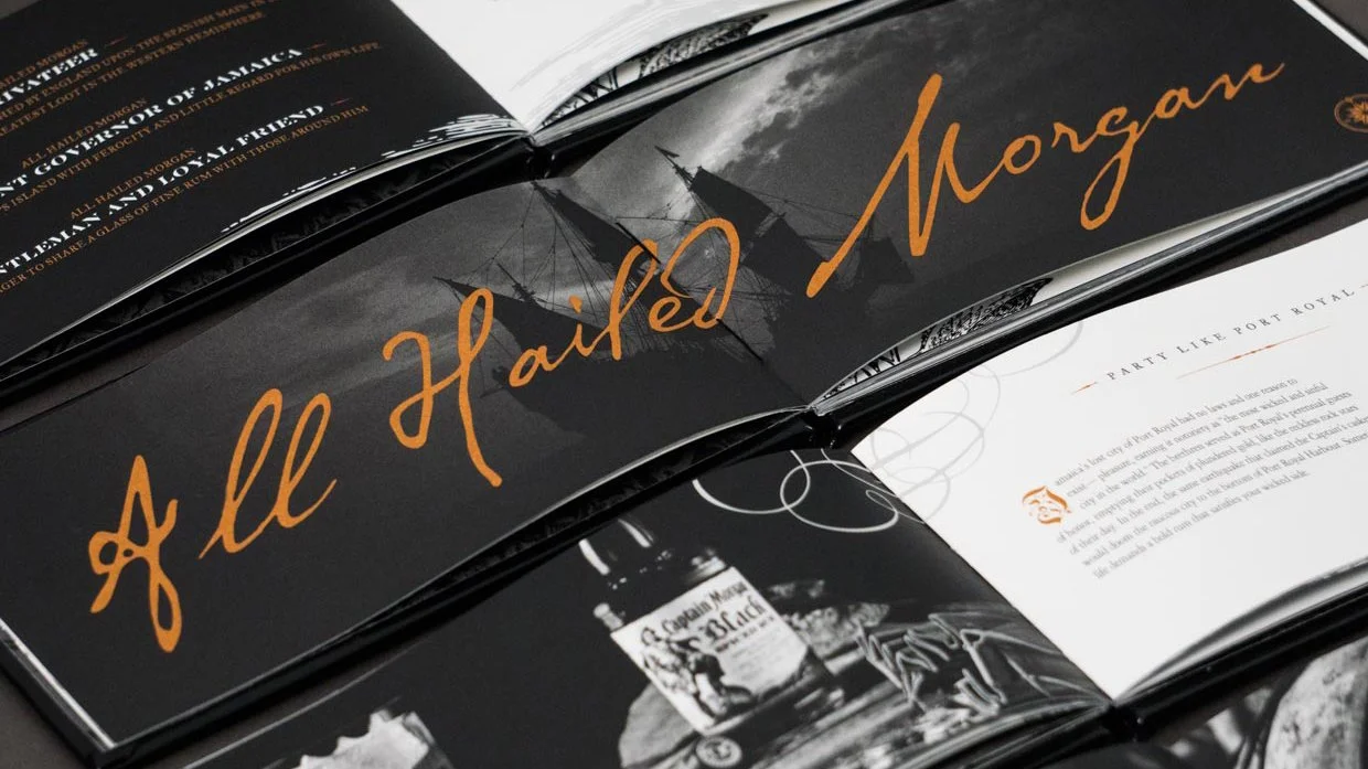 Overlapping Captain Morgan Black brand-book spreads with monochrome imagery and copper All Hail Morgan lettering.