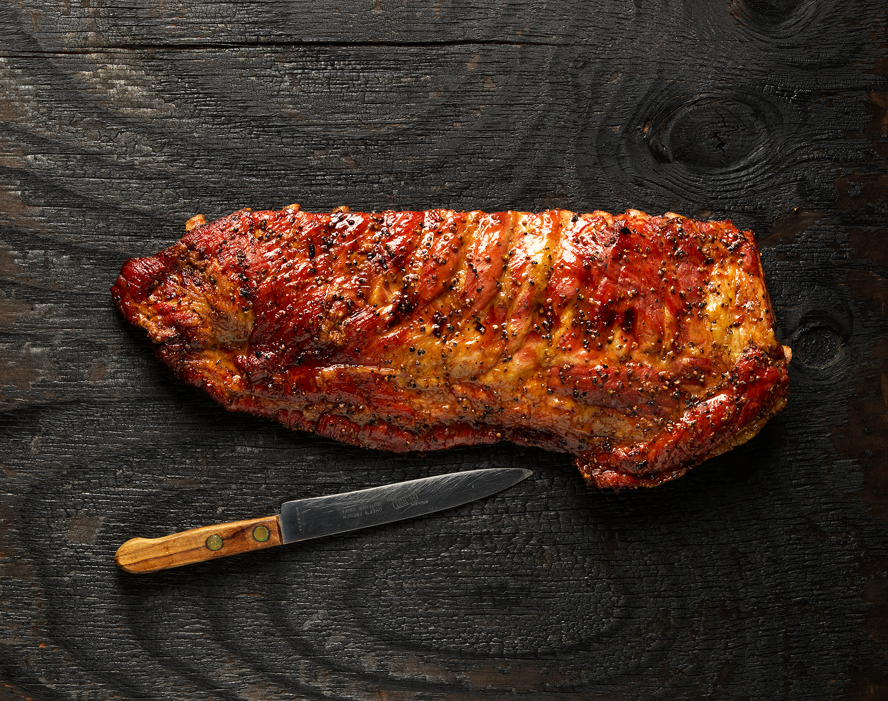 Hill Country rack of glazed ribs on dark wood with a knife beside it.