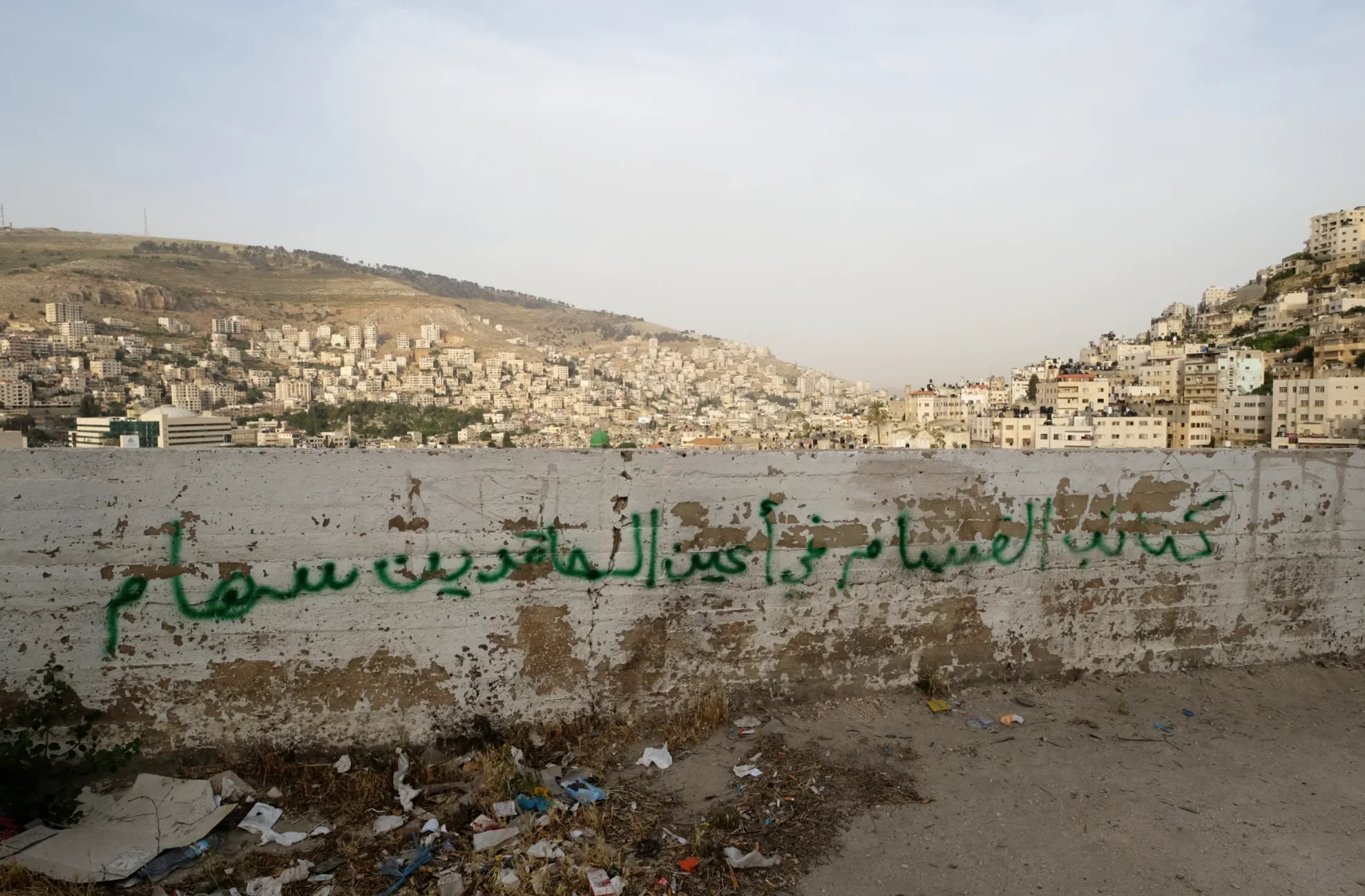 A hilltop view of the Palestinian city Nablus, marked by graffiti that reads,  "Al-Qassam brigade is an arrow in spiteful's eyes." Al-Qassam is the military wing of the Palestinian Hamas organization. The message is directed towards both the Palestin