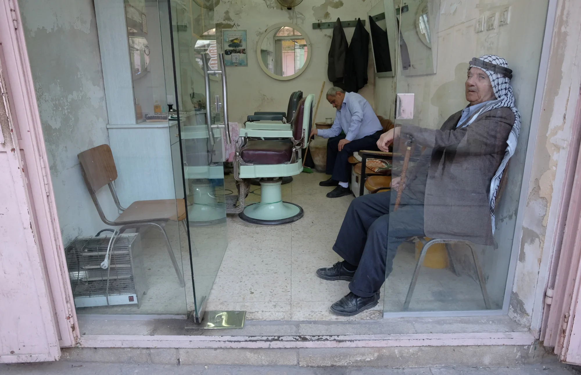 Hebron's Old Quarter has been nicknamed 'Ghost Town' after the area was declared an H2 military zone in 2015. Many shops were forced to close, but a few remain. These men watch passers-by from inside a barbershop.