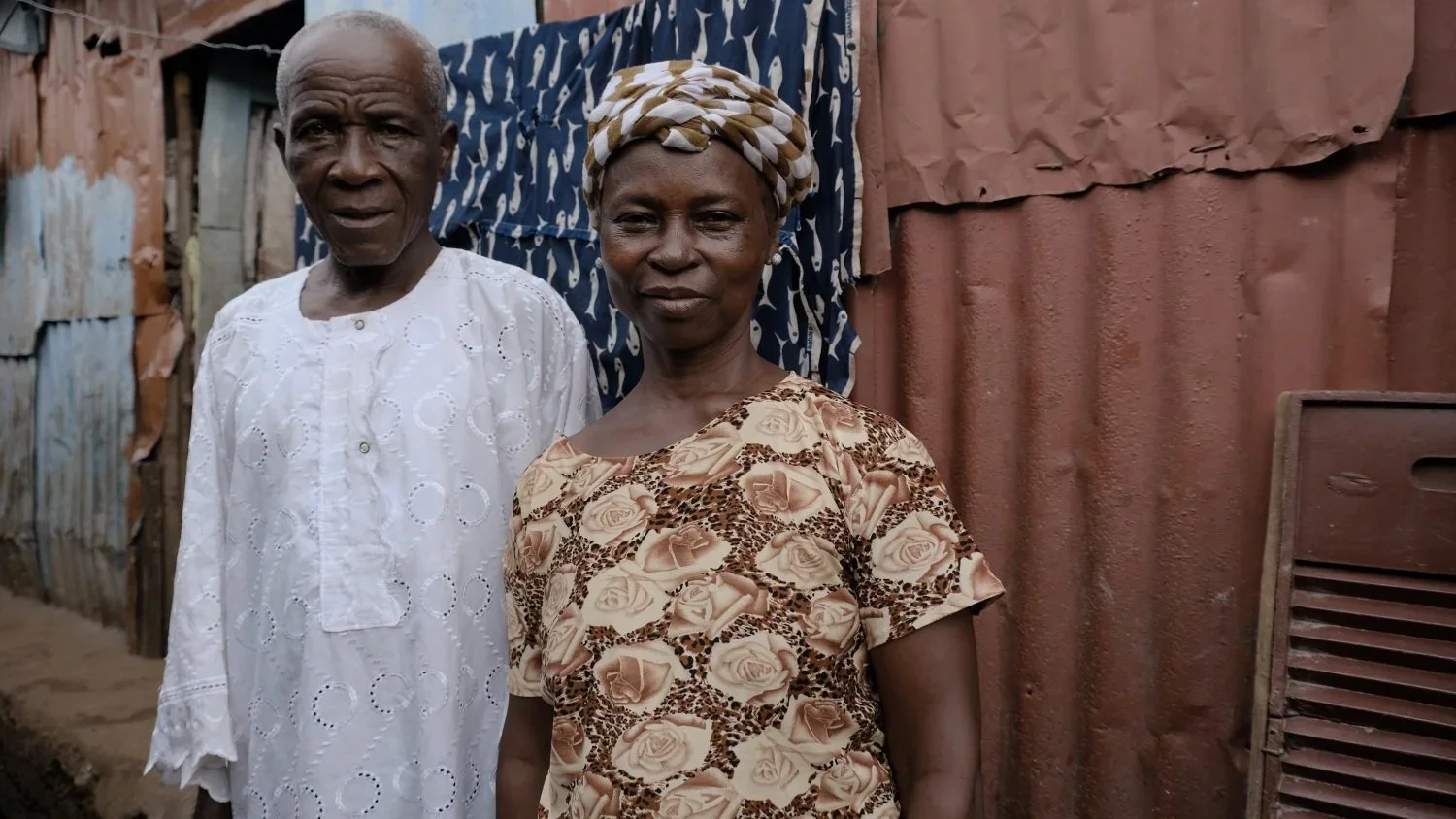 Mahawa and Pa Morlai Kamara. Wife and husband Mahawa and Pa Morlai stand outside their home in the community in Kroo Bay. They have five children and started a business selling African meat soup to support the family. They struggle to make enough inc