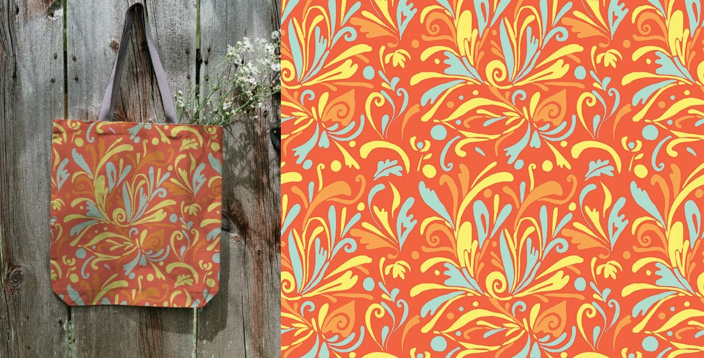 A fabric tote bag with an orange, yellow, and light blue floral pattern hanging on a wooden fence with some white flowers nearby.