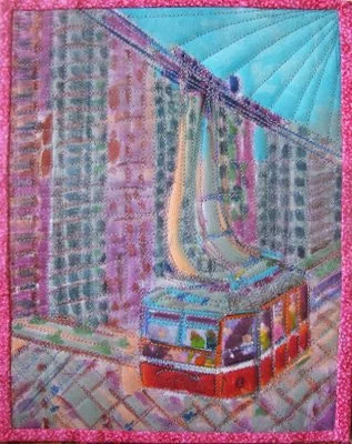 A close-up view of a colorful quilt depicting a city bus with tall buildings in the background, featuring pink, blue, purple, and turquoise tones.