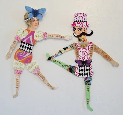 Two paper-crafted characters with colorful outfits and accessories, one with a blue bow and one with a pink hat, posed against a plain background.
