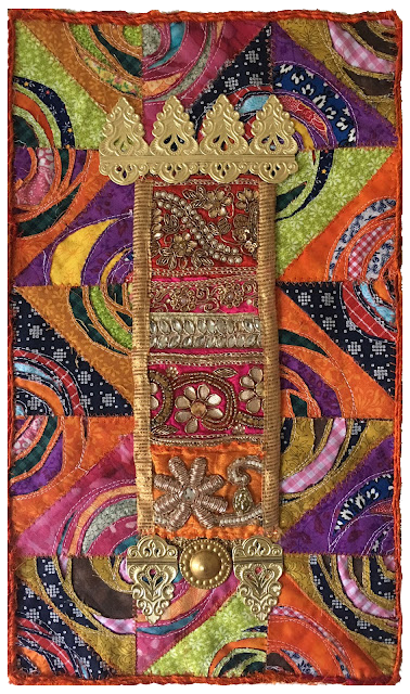 Colorful patchwork fabric with intricate gold and silver embroidery, featuring a vertical decorative element with floral and ornamental motifs.