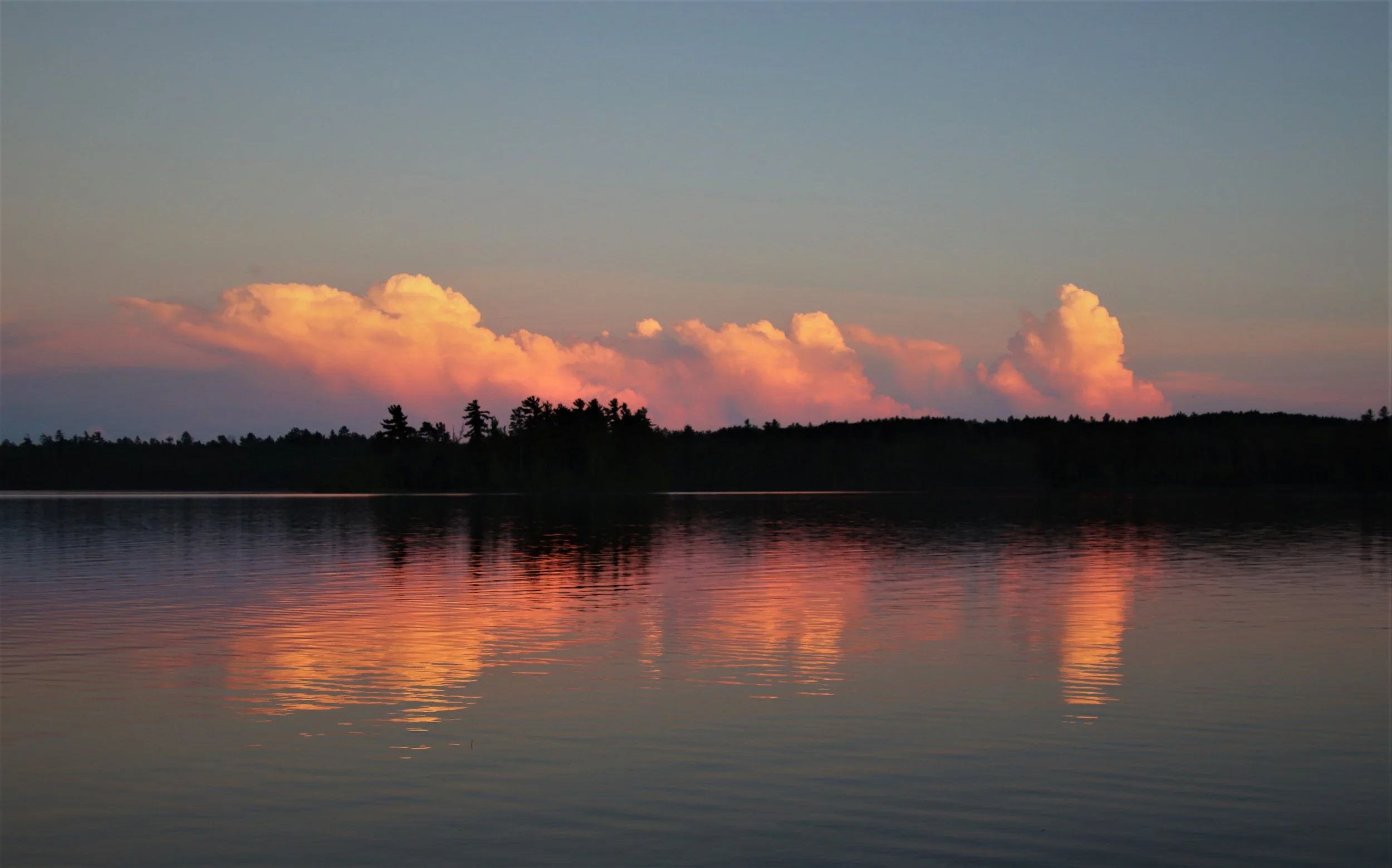Sunset over a lake with cloud reflections and treeline silhouette.