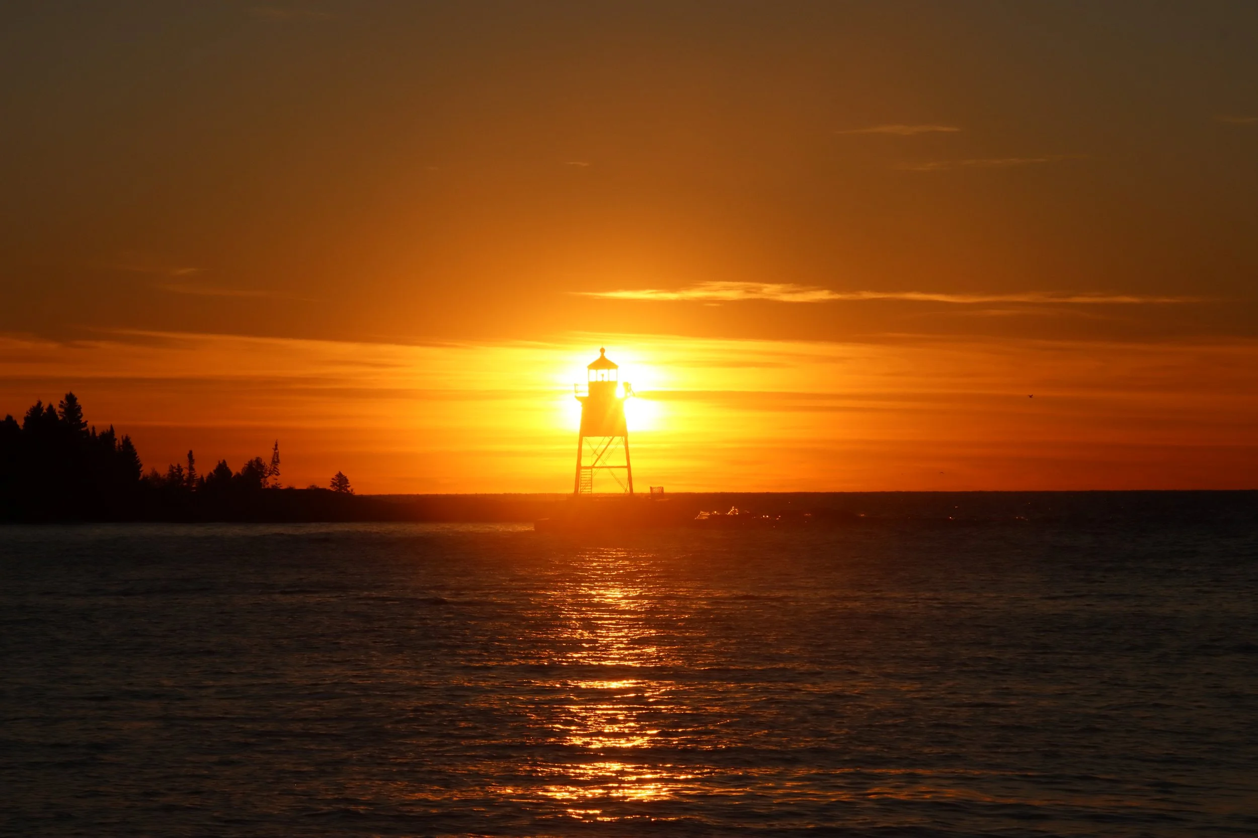 Sunset over a body of water with a lighthouse silhouette in the foreground.