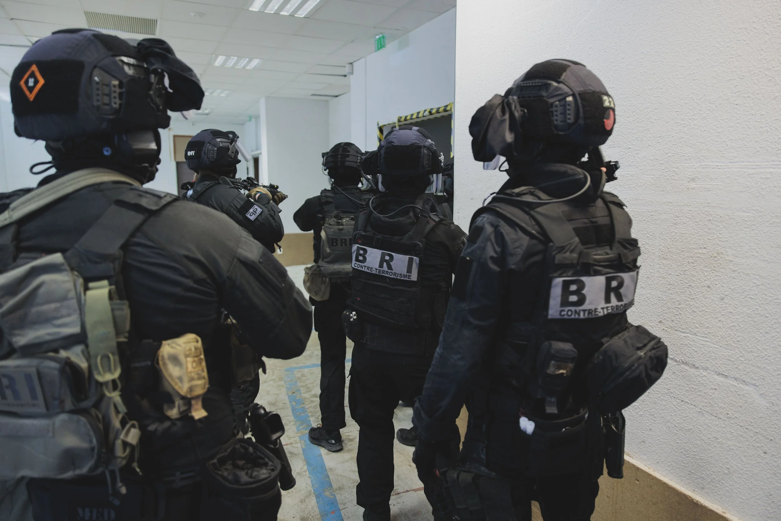 Groupe de membres d'une unité d'intervention de la BRI-PP en tenue tactique, portant des gilets pare-balles et des casques, dans une zone intérieure, probablement lors d'une opération ou d'une entraînement.