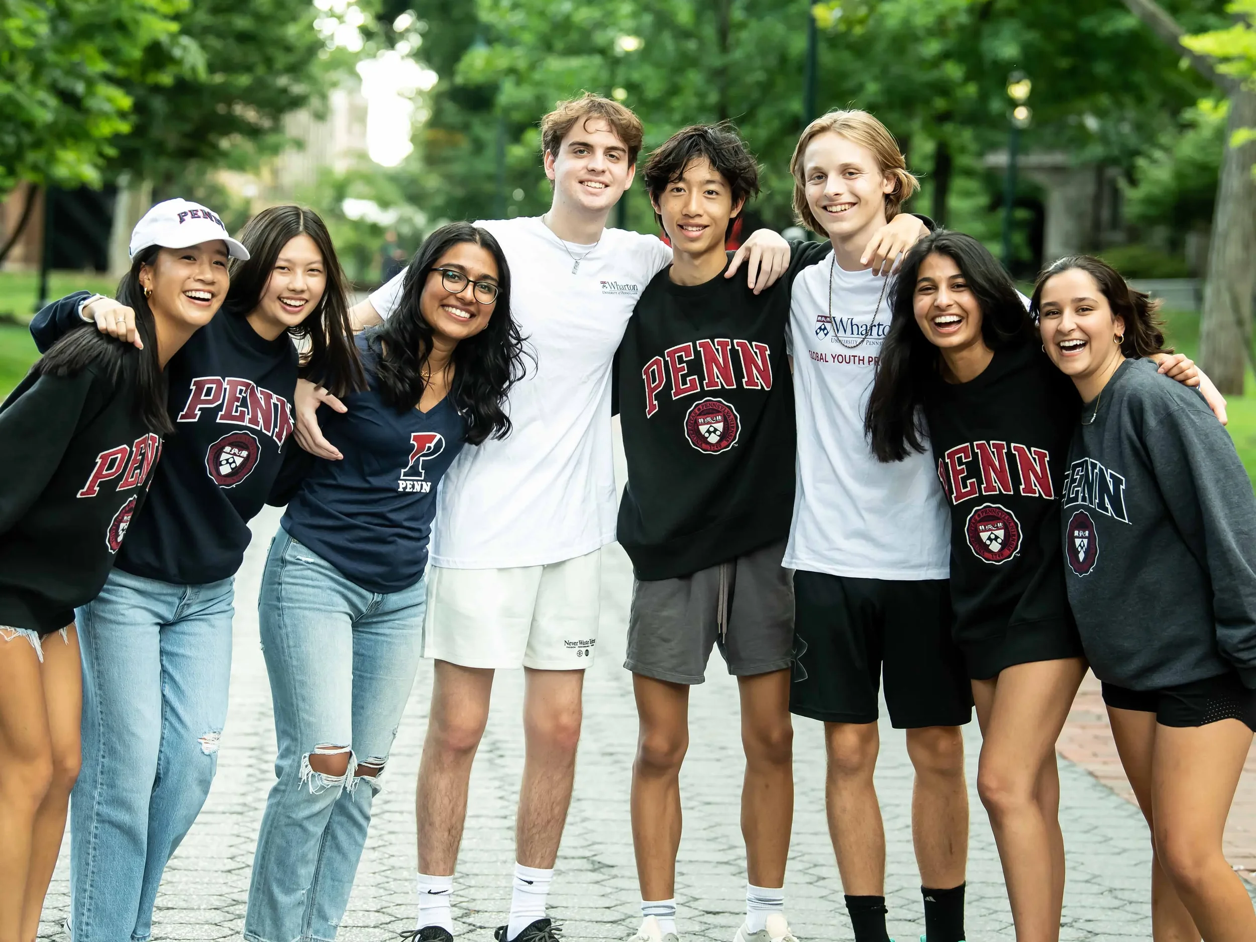 Group of diverse young adults smiling and standing closely together outdoors in a park with green trees in the background.