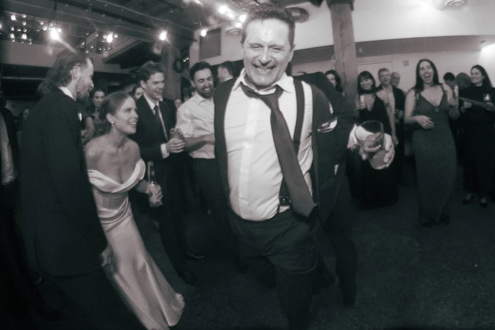 People dancing and enjoying at a party or celebration, some holding drinks, in a lively indoor setting.