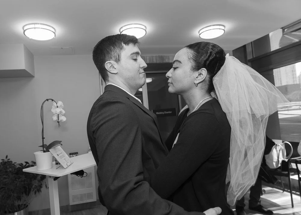 A bride and groom sharing a close dance in a wedding venue, with the bride wearing a veil and pearl necklace.