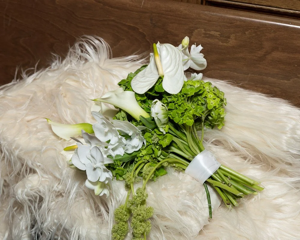 A bouquet of white flowers and green foliage resting on a fluffy cream-colored rug.