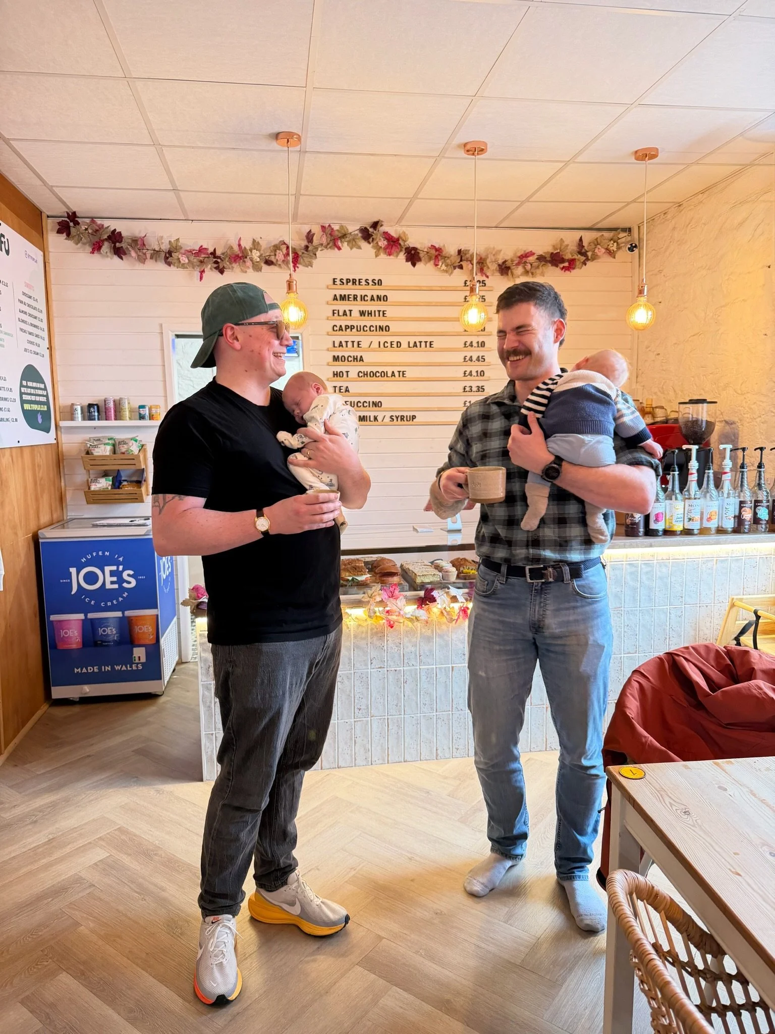 Two dads enjoying a coffee with their babies at Tyfu Play, Cardiff