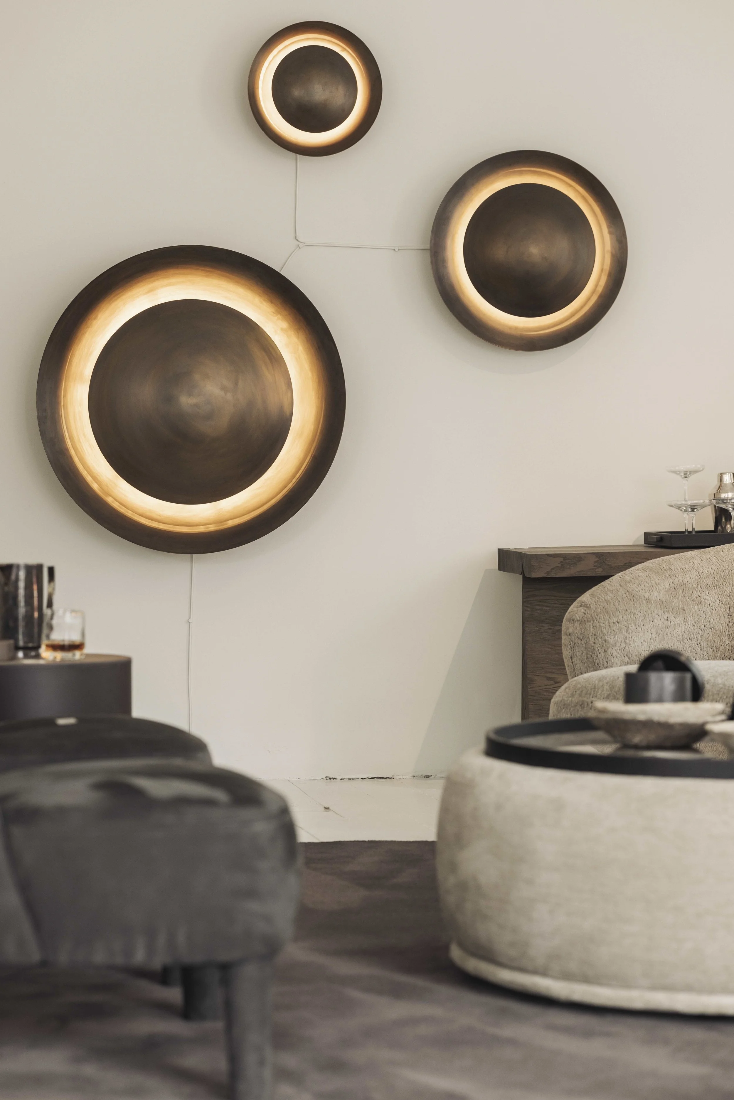 Living room with modern wall-mounted circular light fixtures and a beige sofa. Rounded stone tables with black trays and glassware are in the foreground.