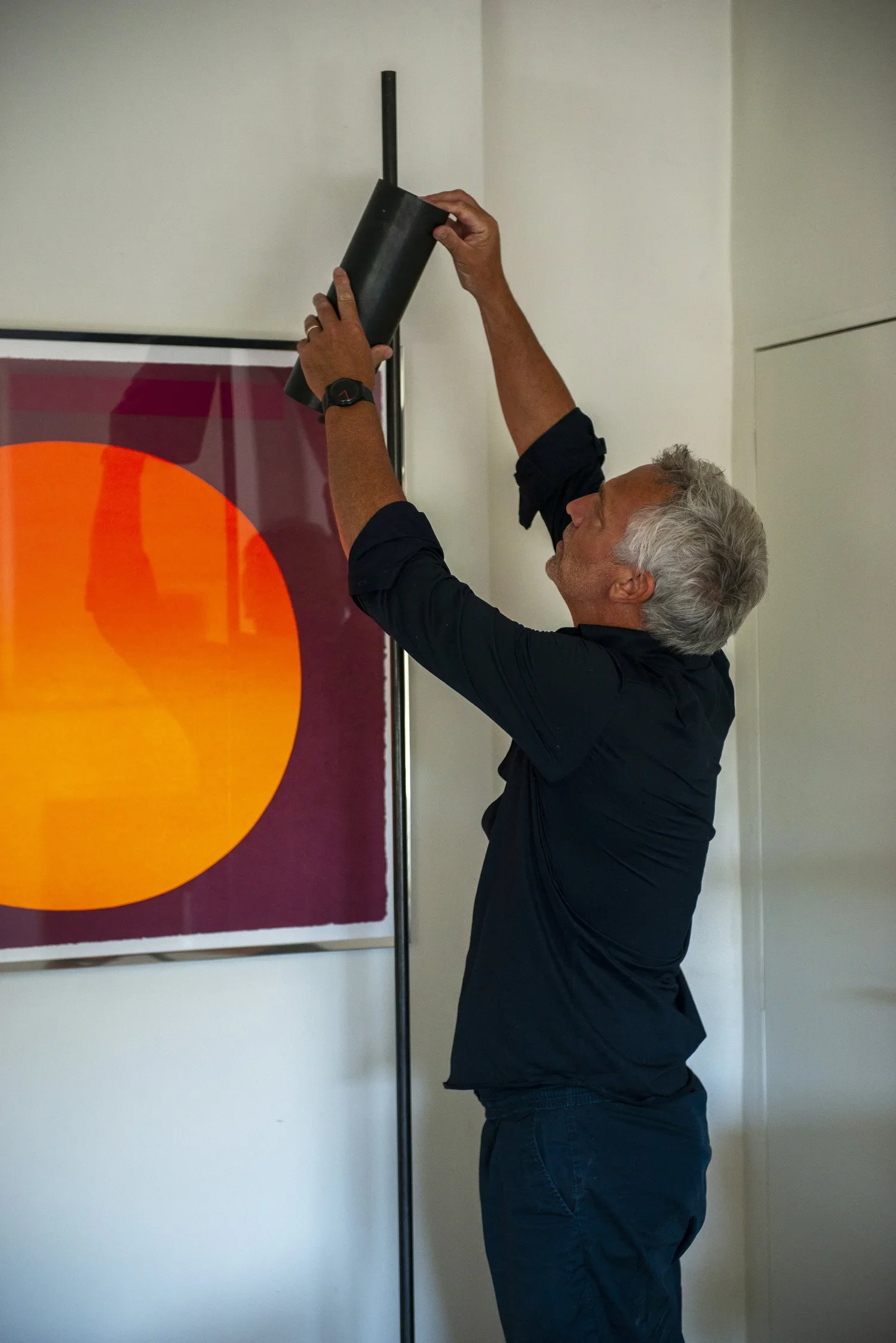 Man adjusting a black pole or tube in an indoor setting, with modern decor and a large abstract artwork on the wall.