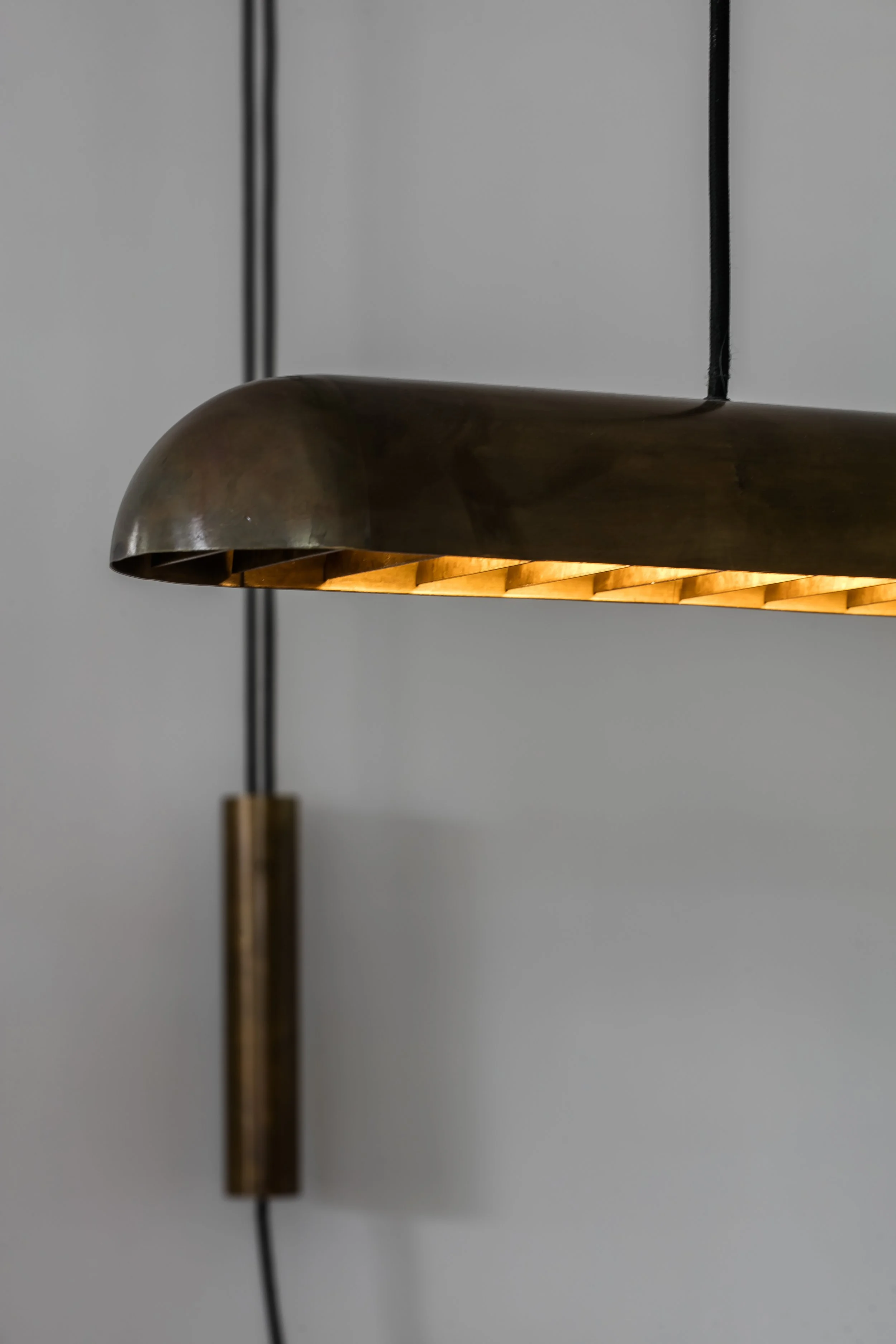 Close-up of a modern hanging pendant light with a metallic shade and warm interior illumination, suspended from a ceiling by black cords.