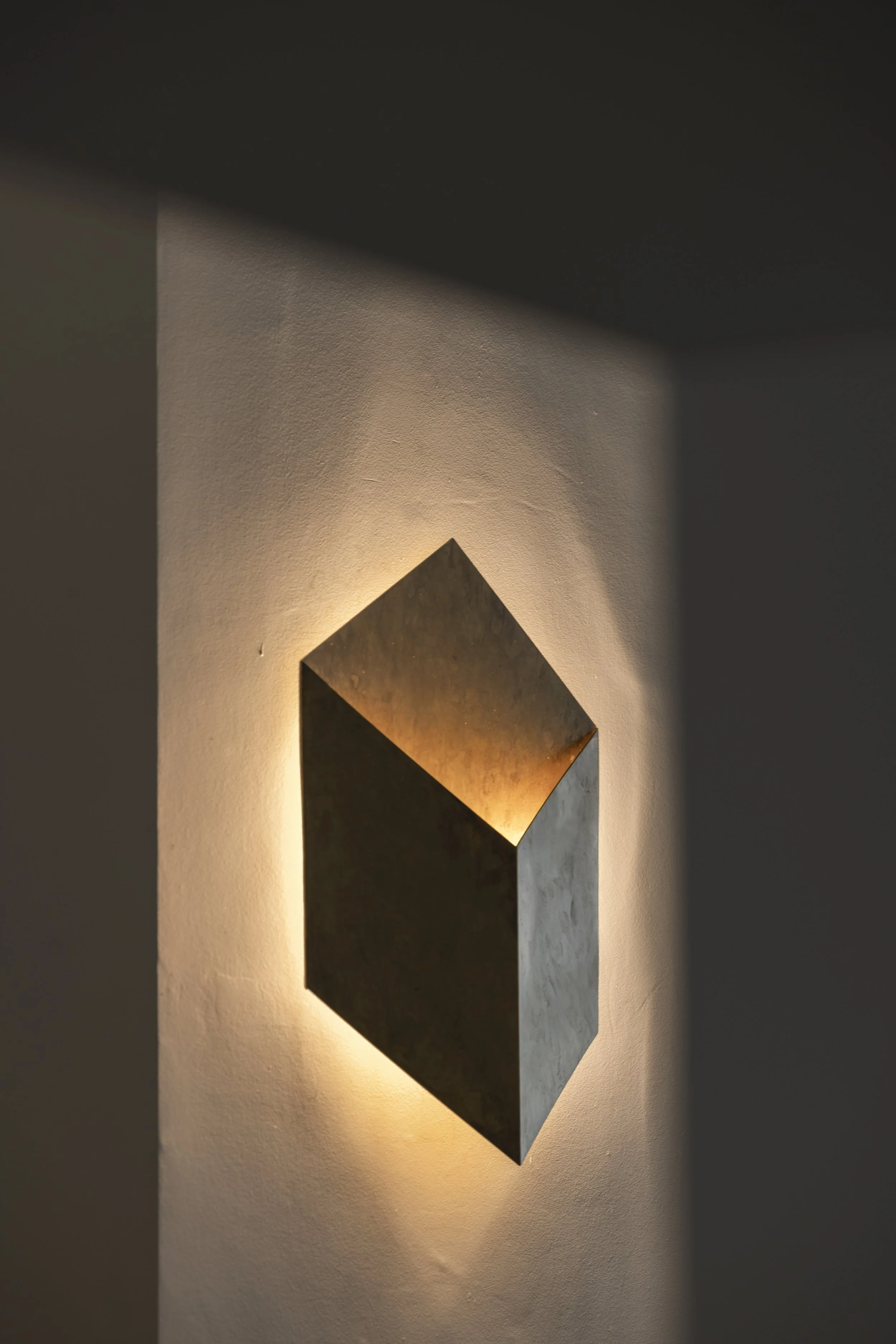 A geometric wall-mounted light fixture cast a soft warm glow on a textured wall in this minimalist interior design.