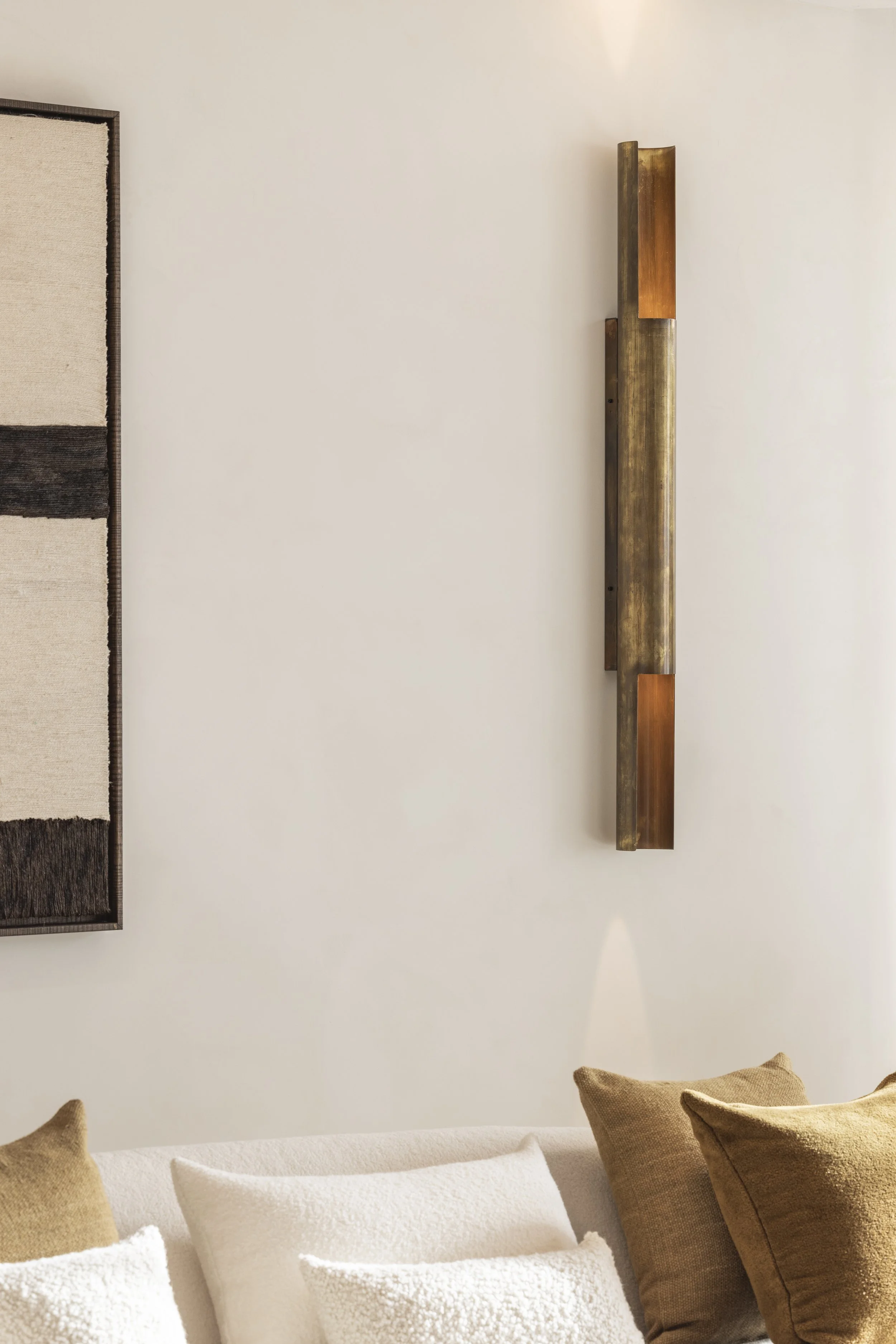 Living room with beige and brown pillows on a white sofa, a textured wall hanging on the wall, and a metal and wood wall sculpture.