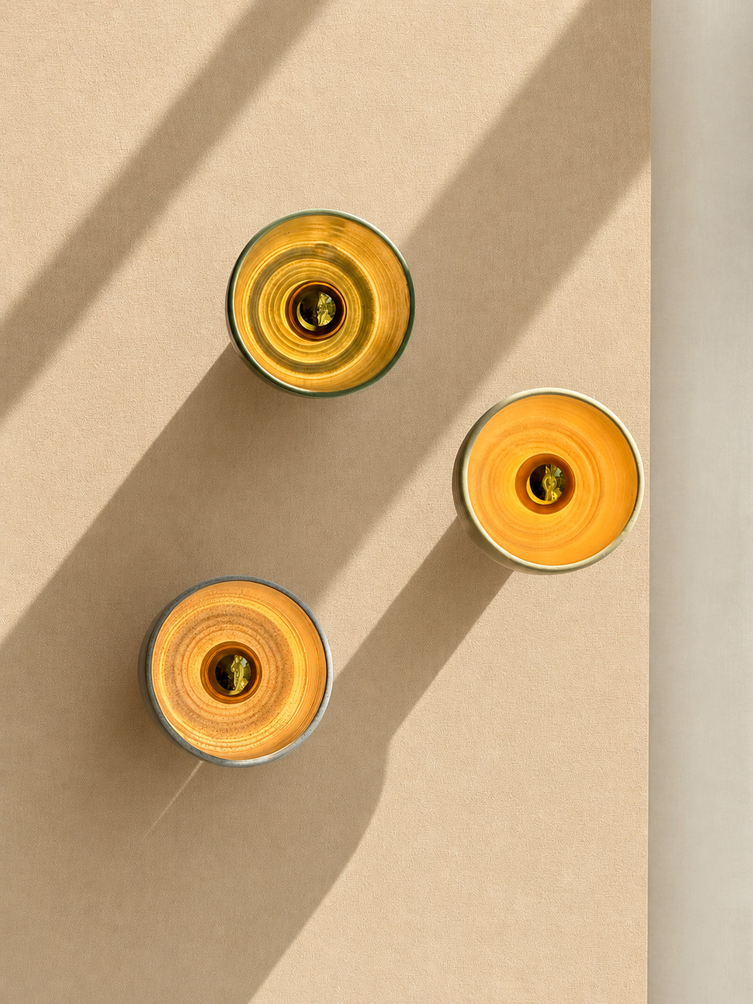 Top-down view of three yellow and orange candles with wicks, casting shadows on a beige surface.