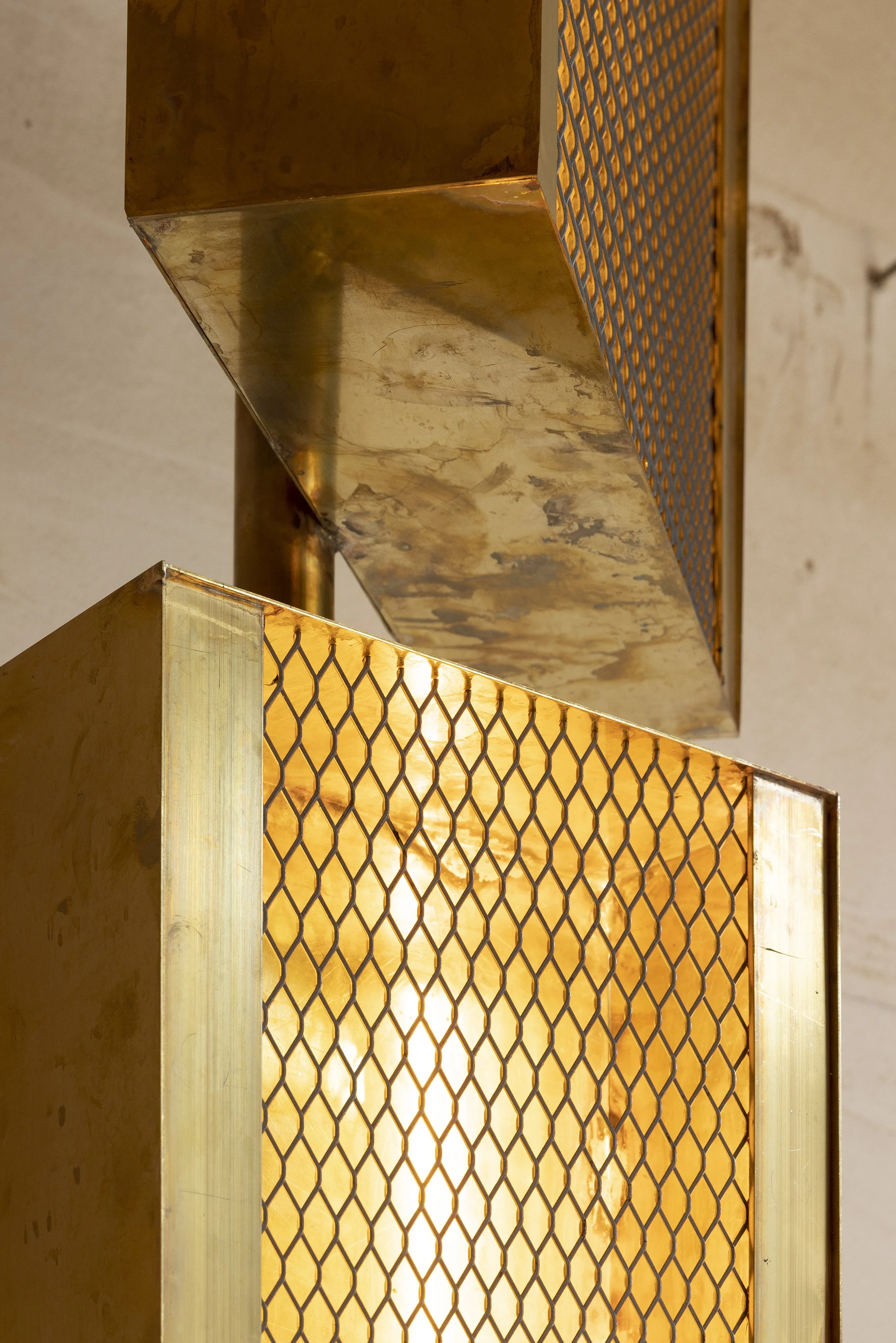 Close-up of a metallic structure with a mesh panel, with warm lighting shining through, against a plain wall.