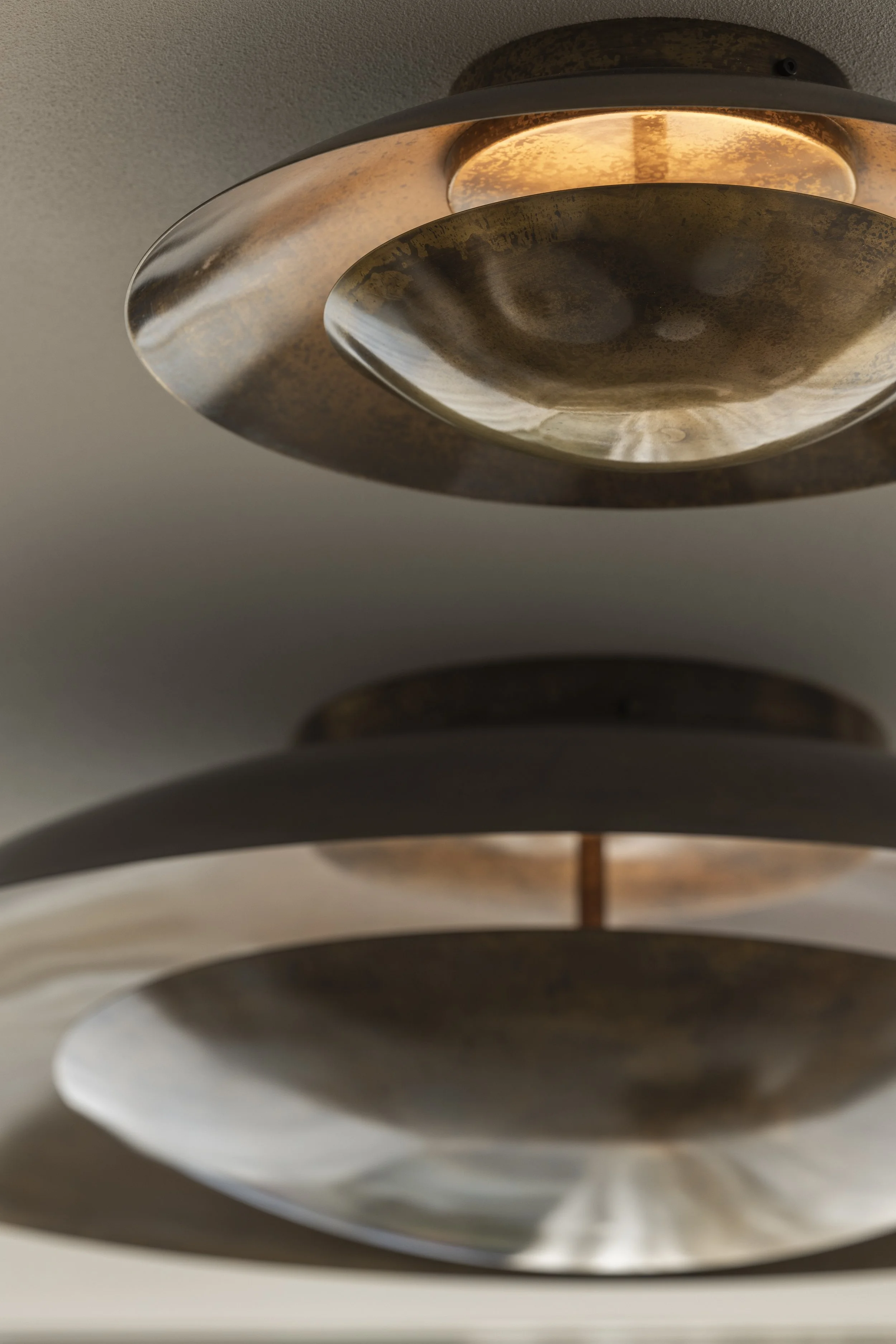 Close-up view of a modern, layered ceiling light fixture with a metallic finish, featuring circular, concentric components with warm internal lighting.
