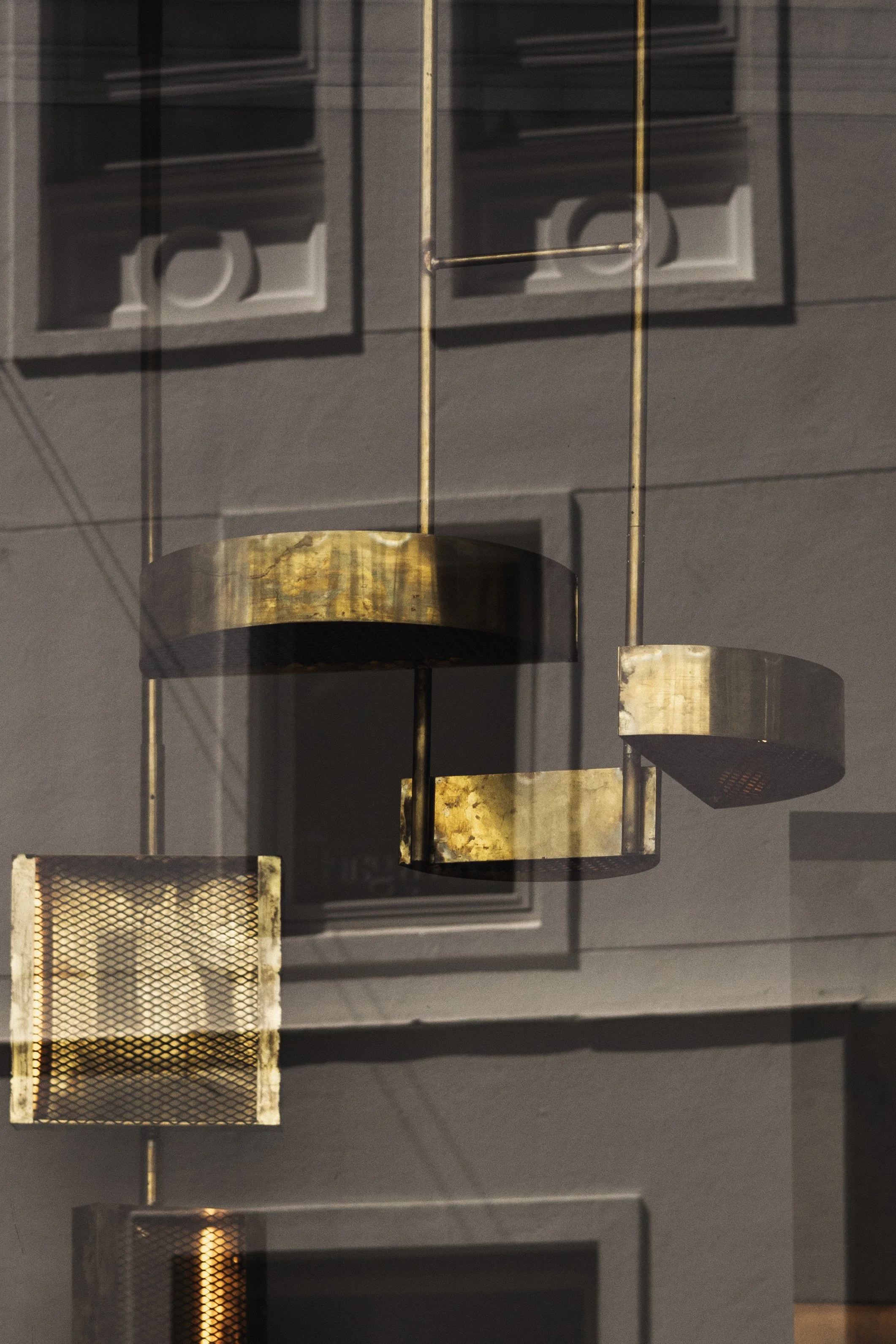 Reflection of a chandelier with cylindrical gold-colored shades and metal mesh panels on a glass surface.
