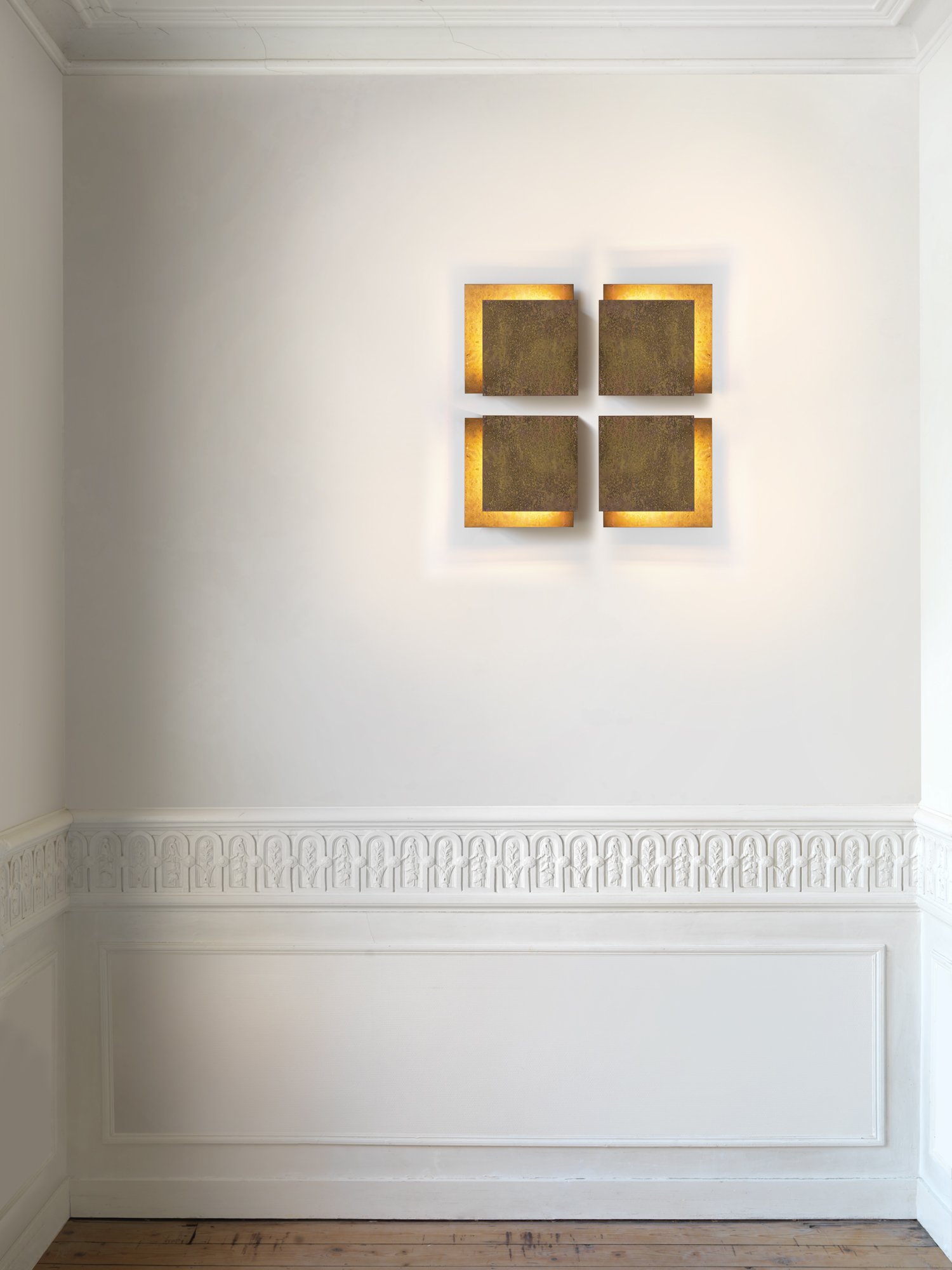 Empty white wall with decorative crown molding at the bottom and a four-piece wall art piece in the center, illuminated with warm backlighting.
