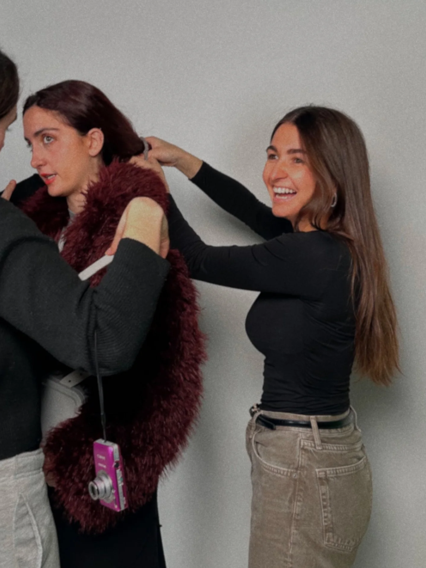 Tres personas ajustando la ropa de una mujer con chaqueta de piel y camiseta negra, mientras sonríe.