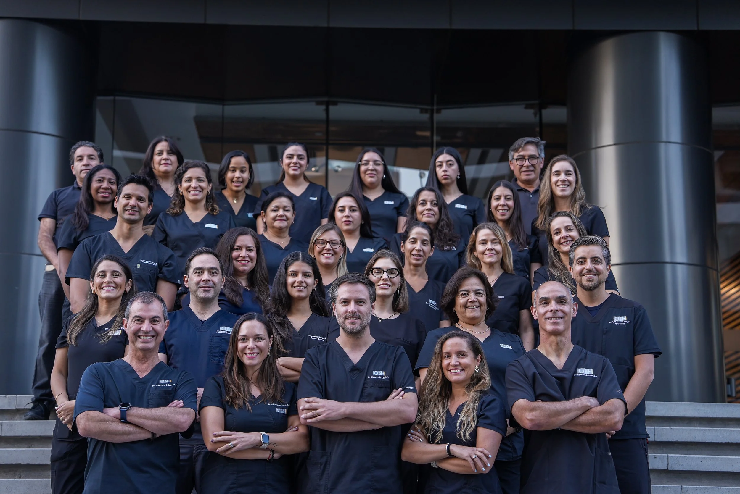 Grupo de profesionales en uniformes oscuros, posando en las escaleras de un edificio moderno con fachada de vidrio.