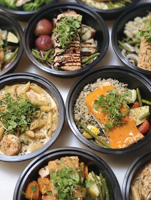 Several bowls of prepared salads and pasta dishes with fresh greens, grilled chicken, vegetables, meats, and sauce garnishes.