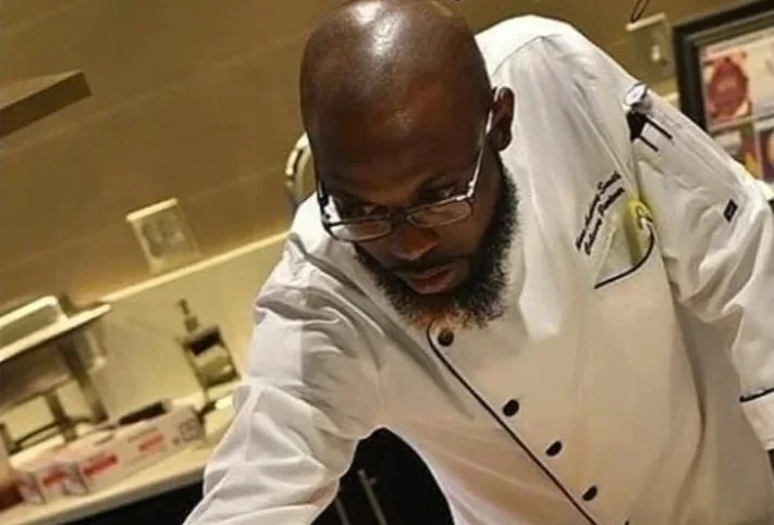 A male chef with glasses and a beard is preparing food in a commercial kitchen.