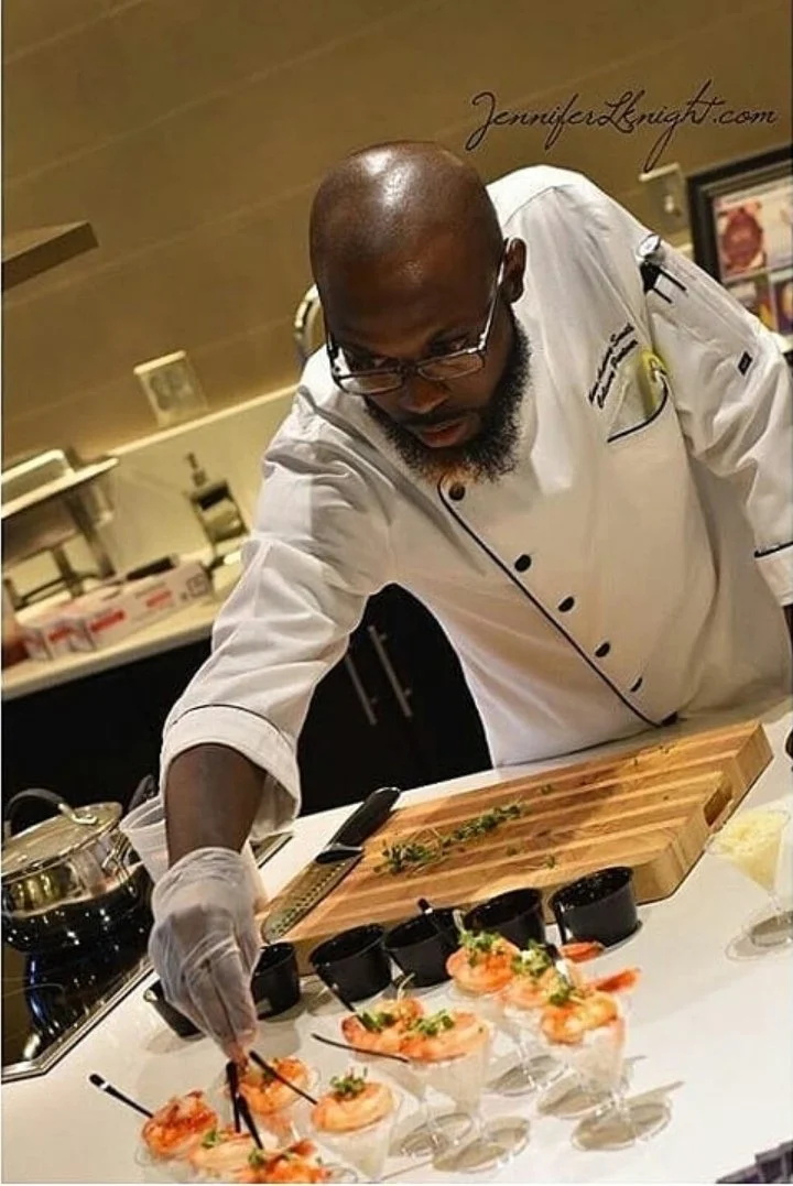 A chef garnishing dishes with shrimp and herbs in a professional kitchen.