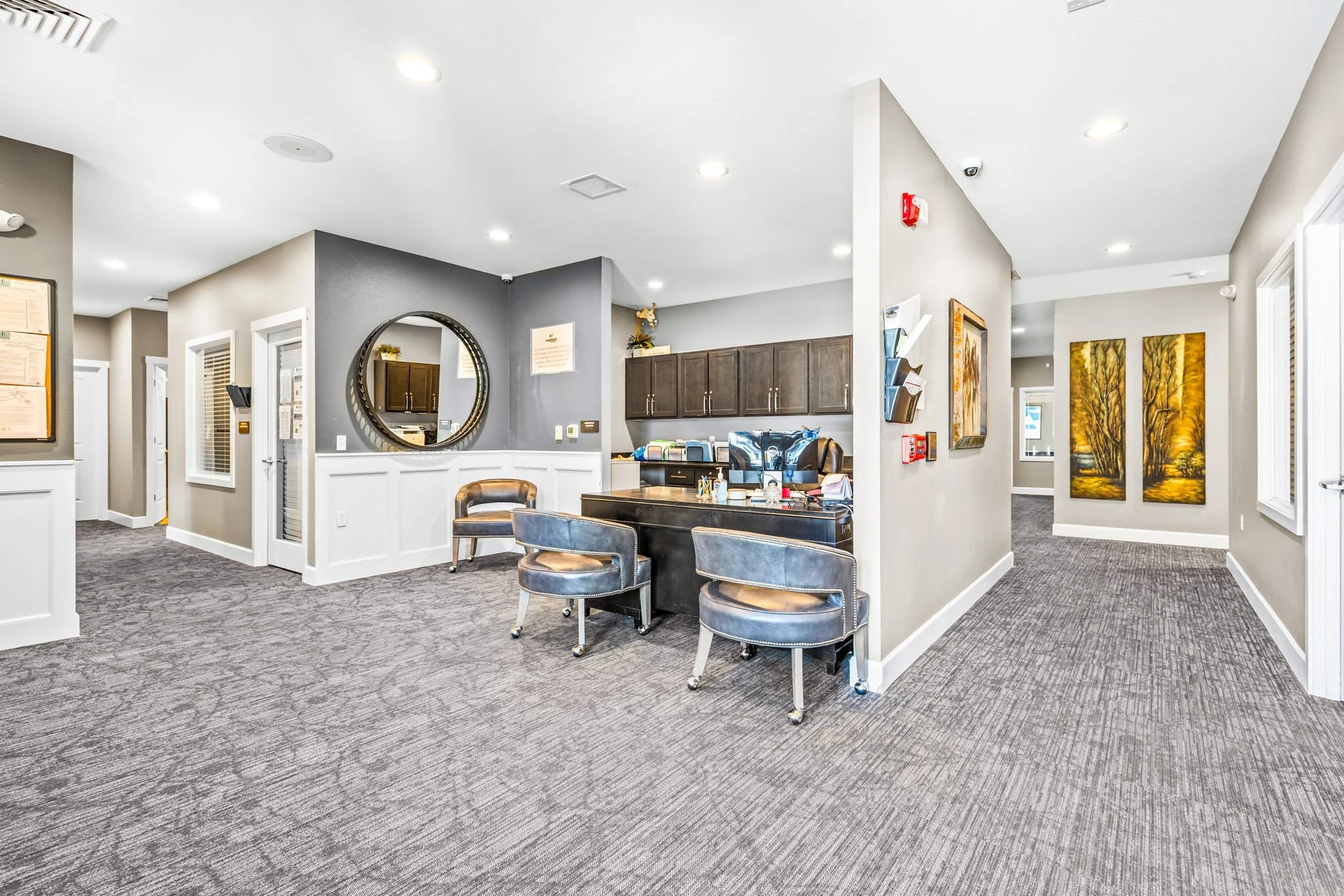 Interior of an office reception area with a desk, chairs, artwork on the walls, and a mirror.