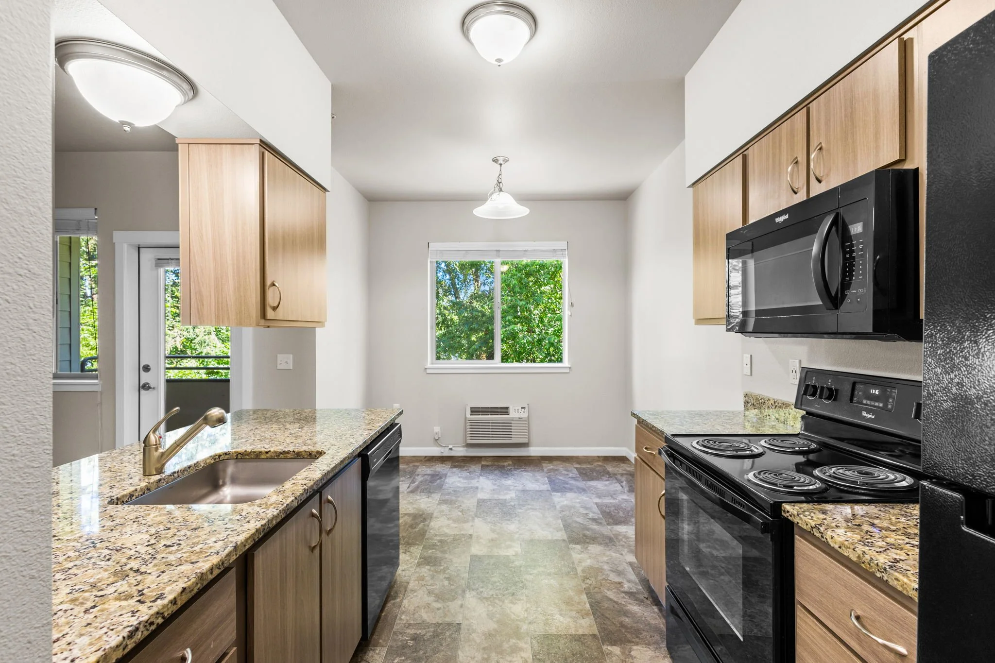 Kitchen with light wood cabinets, granite countertops, black stove, microwave, and a window with outside greenery.