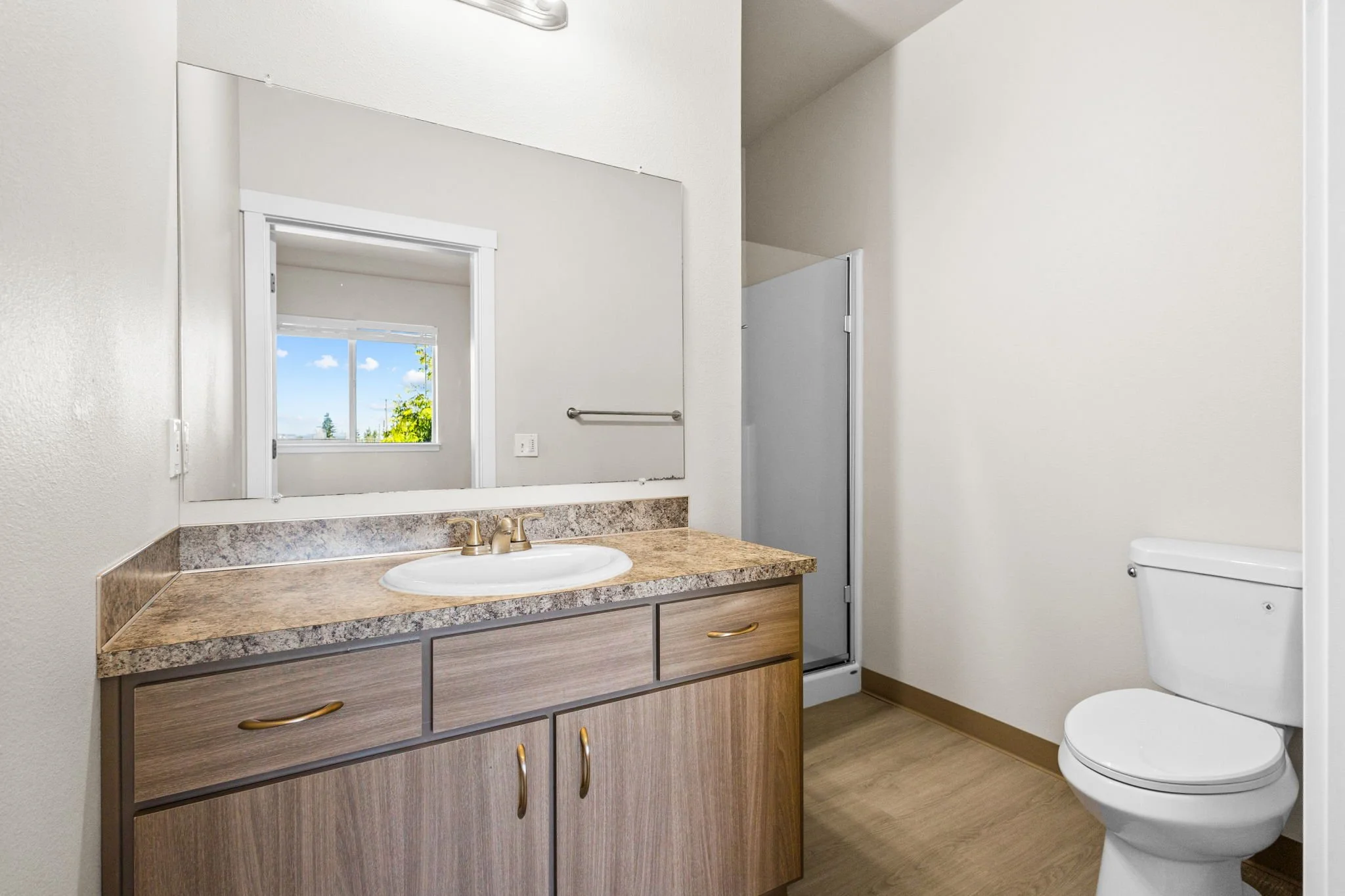 A bathroom with a wooden vanity, granite countertop, sink, large mirror, window, and toilet.