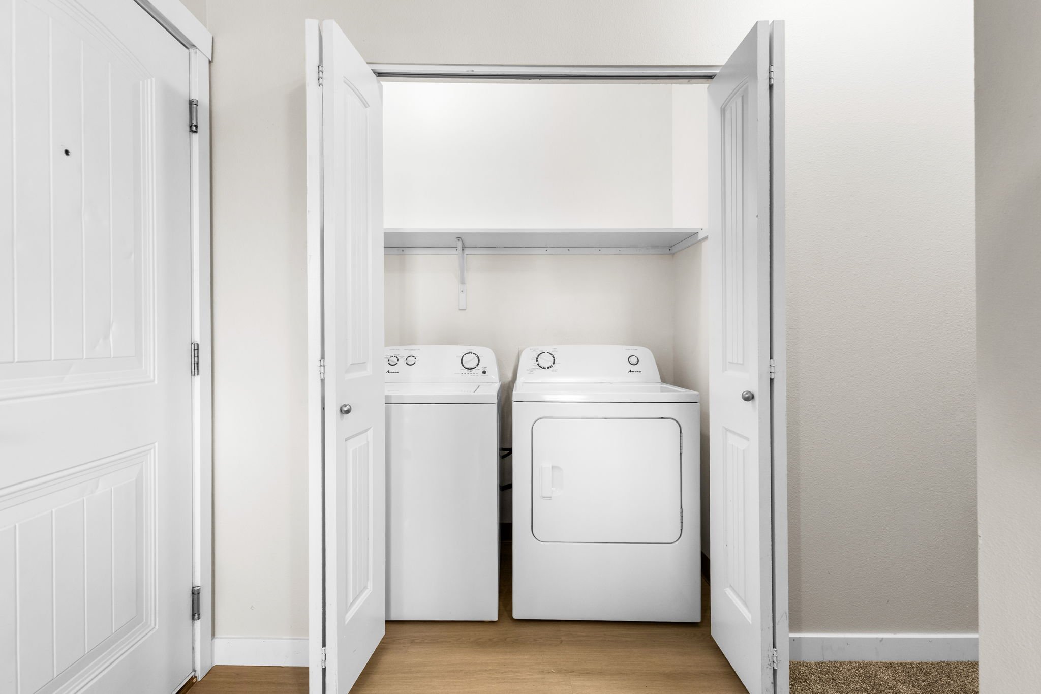 Open closet doors revealing a stacked washer and dryer in a laundry area with white walls and wood flooring.