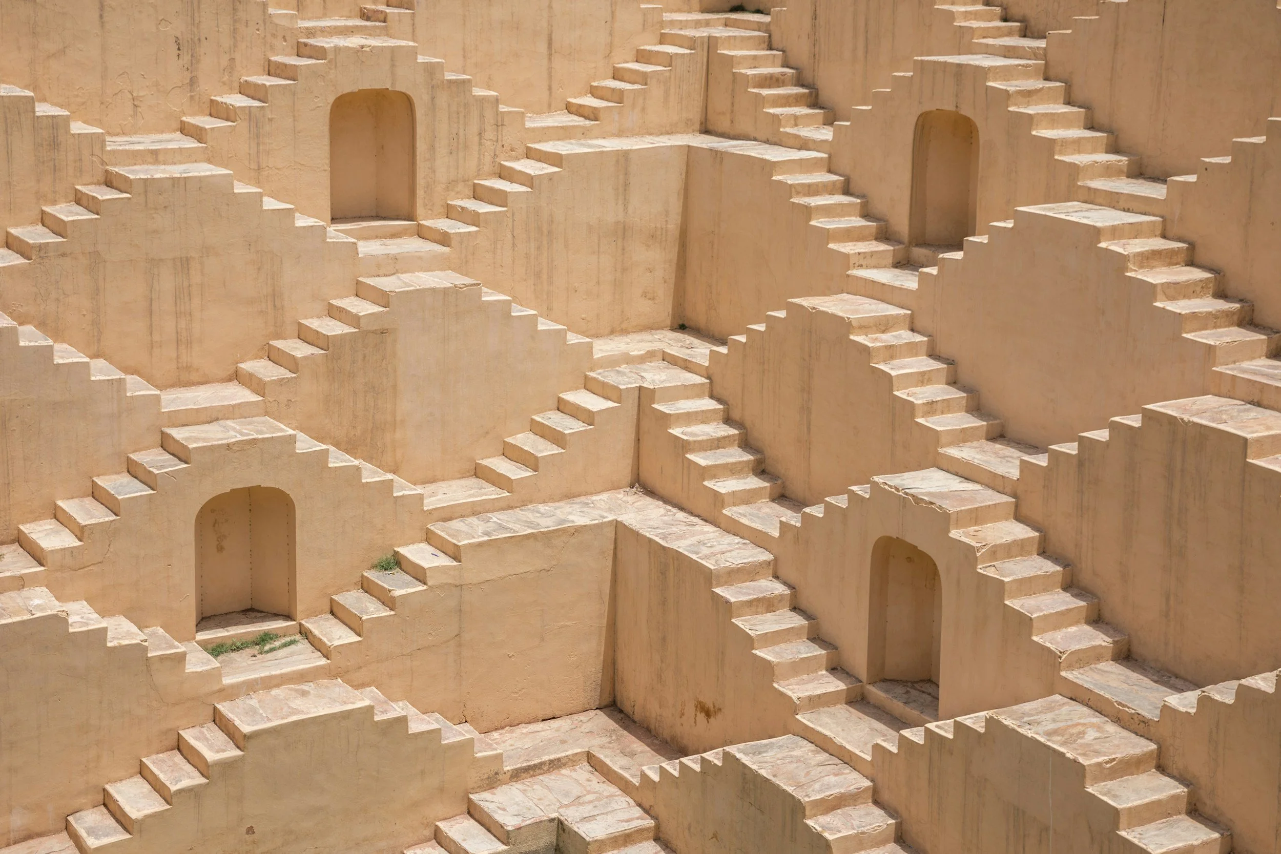 Multiple beige staircases and doorways built into a large tan wall, creating a maze-like structure.