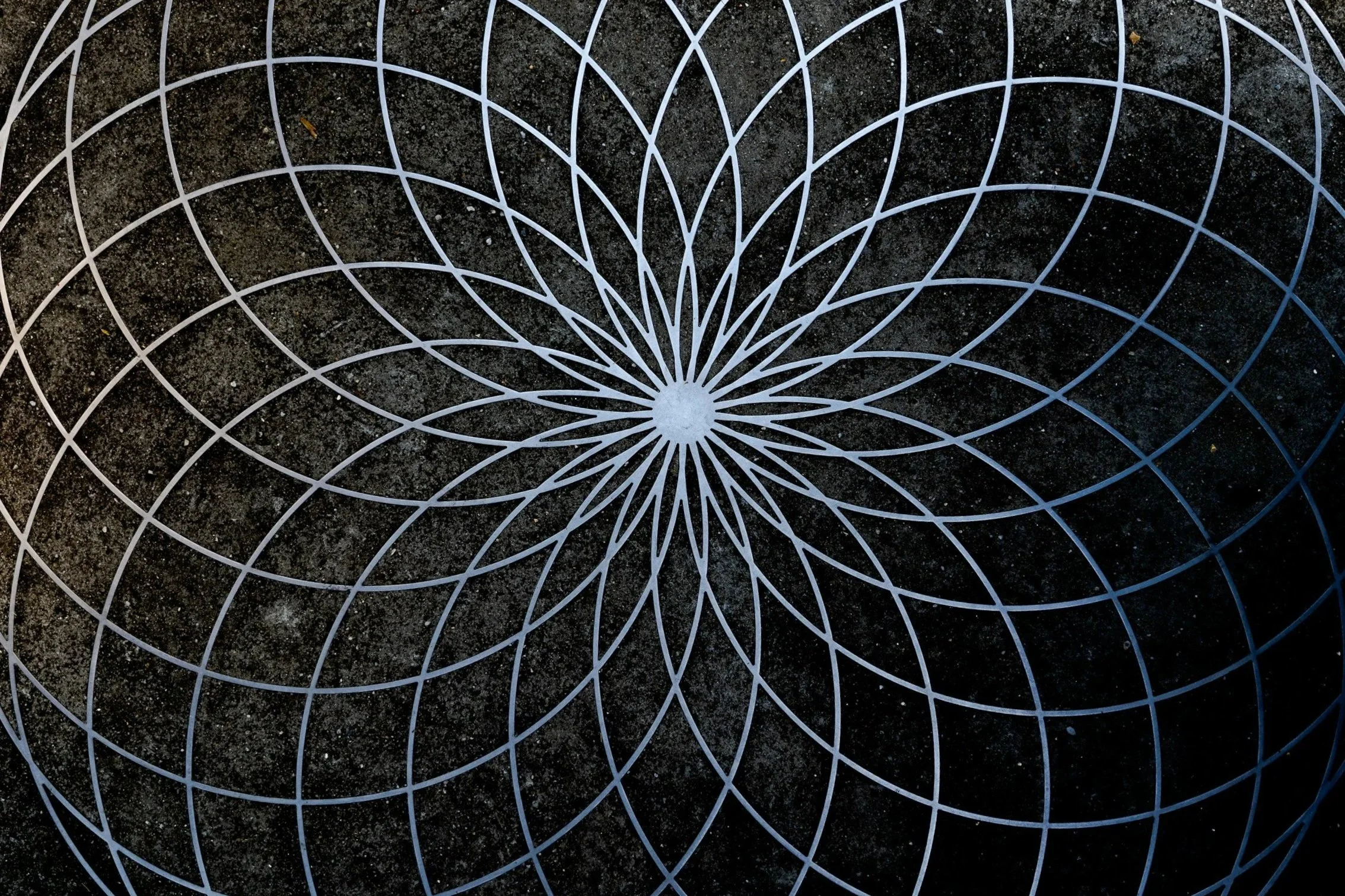 A white geometric pattern resembling a flower, drawn with lines on dark pavement.