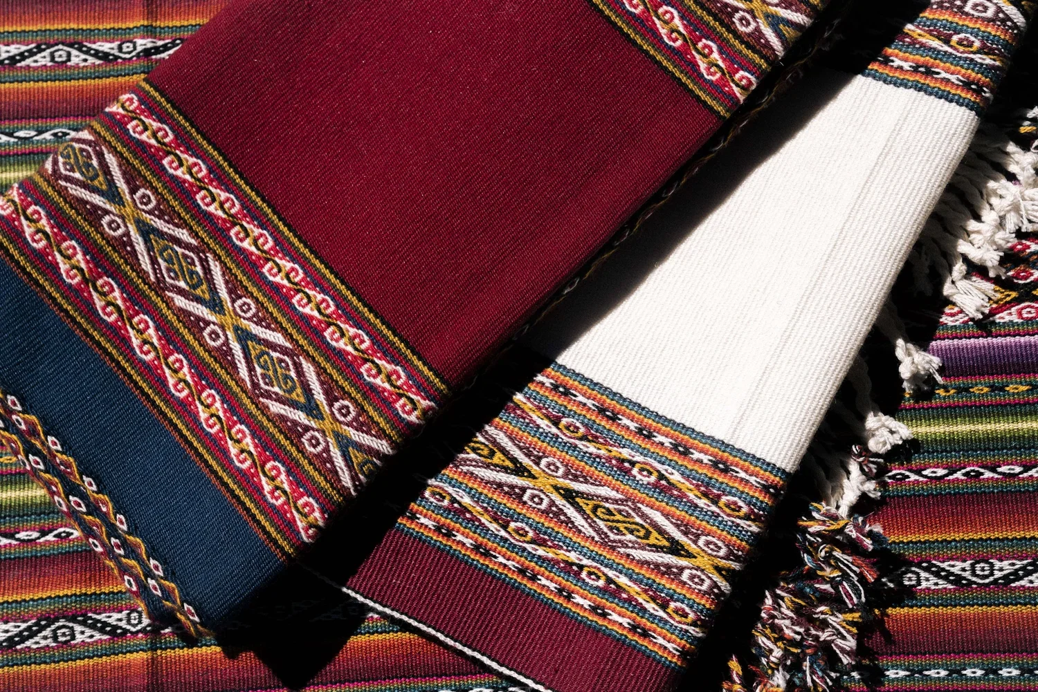 Colorful traditional woven textiles with intricate geometric patterns and fringed edges, featuring red, white, blue, and multicolored stripes.